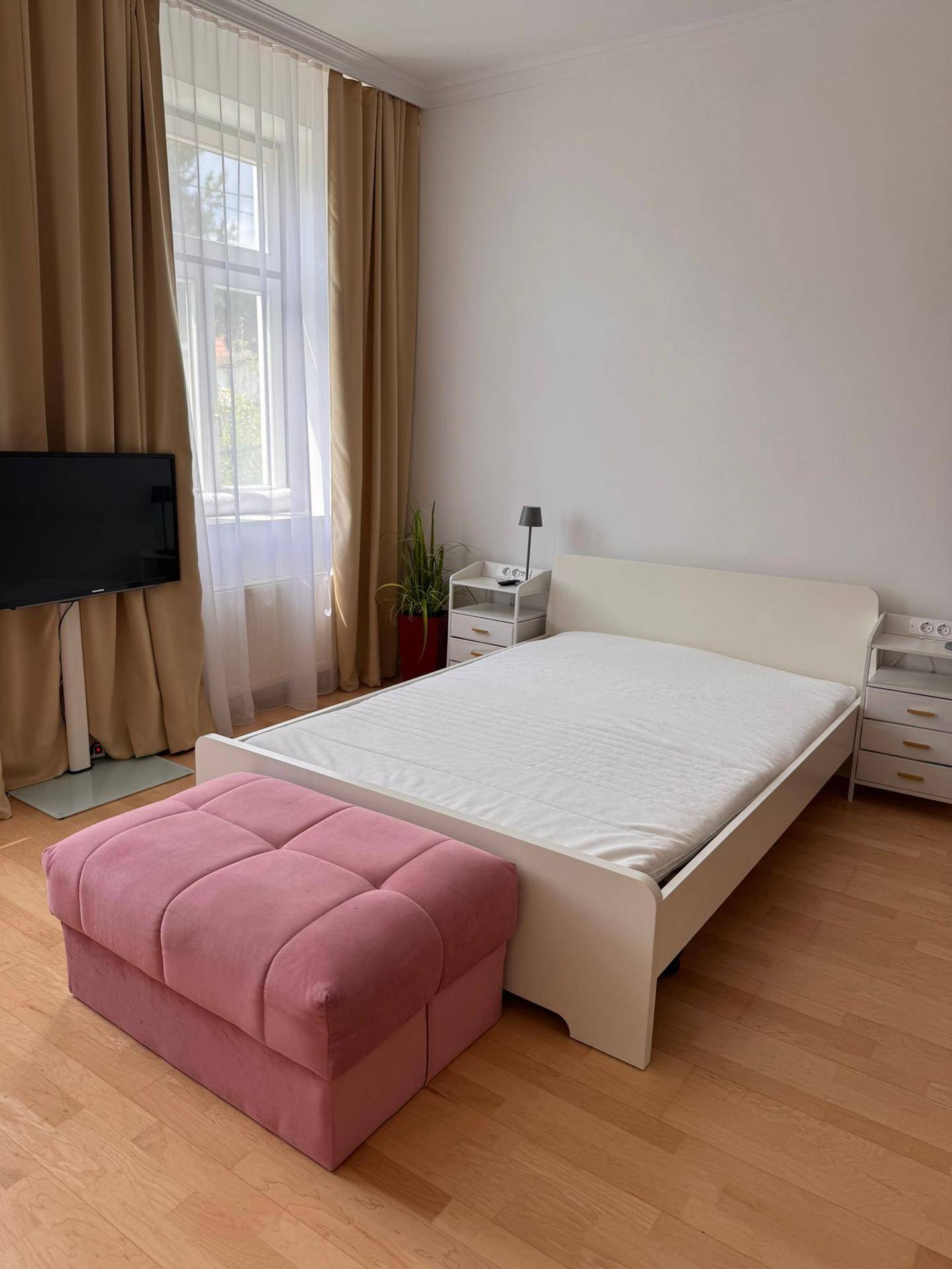Helles Schlafzimmer mit Doppelbett, Nachttischen und großem Fenster mit Vorhängen.