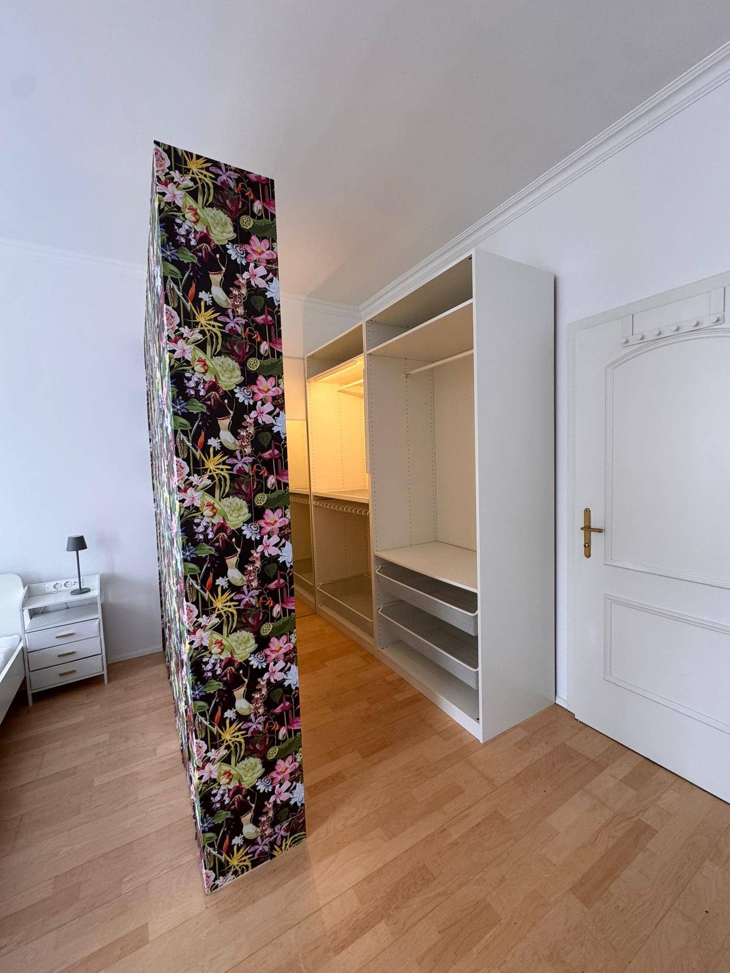 Detailansicht des floral gemusterten Raumteilers und des offenen Schranksystems im Schlafzimmer.
