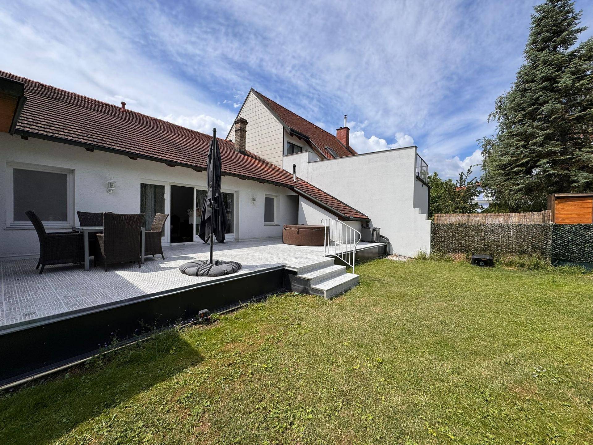 Hinteransicht des Hauses mit großer Terrasse, Rasenfläche und Zugang zum Garten.