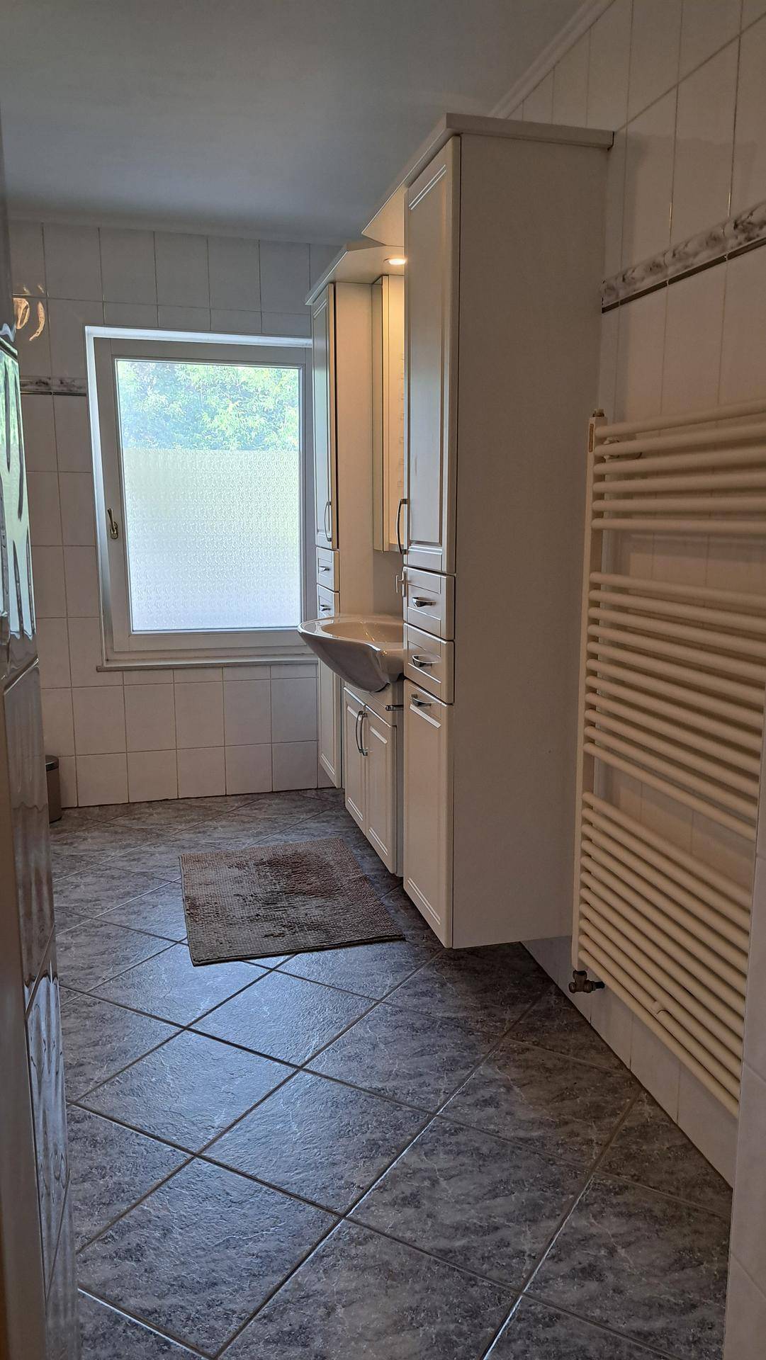 Badezimmer mit Fenster, Waschtischunterschrank und beheiztem Handtuchhalter.