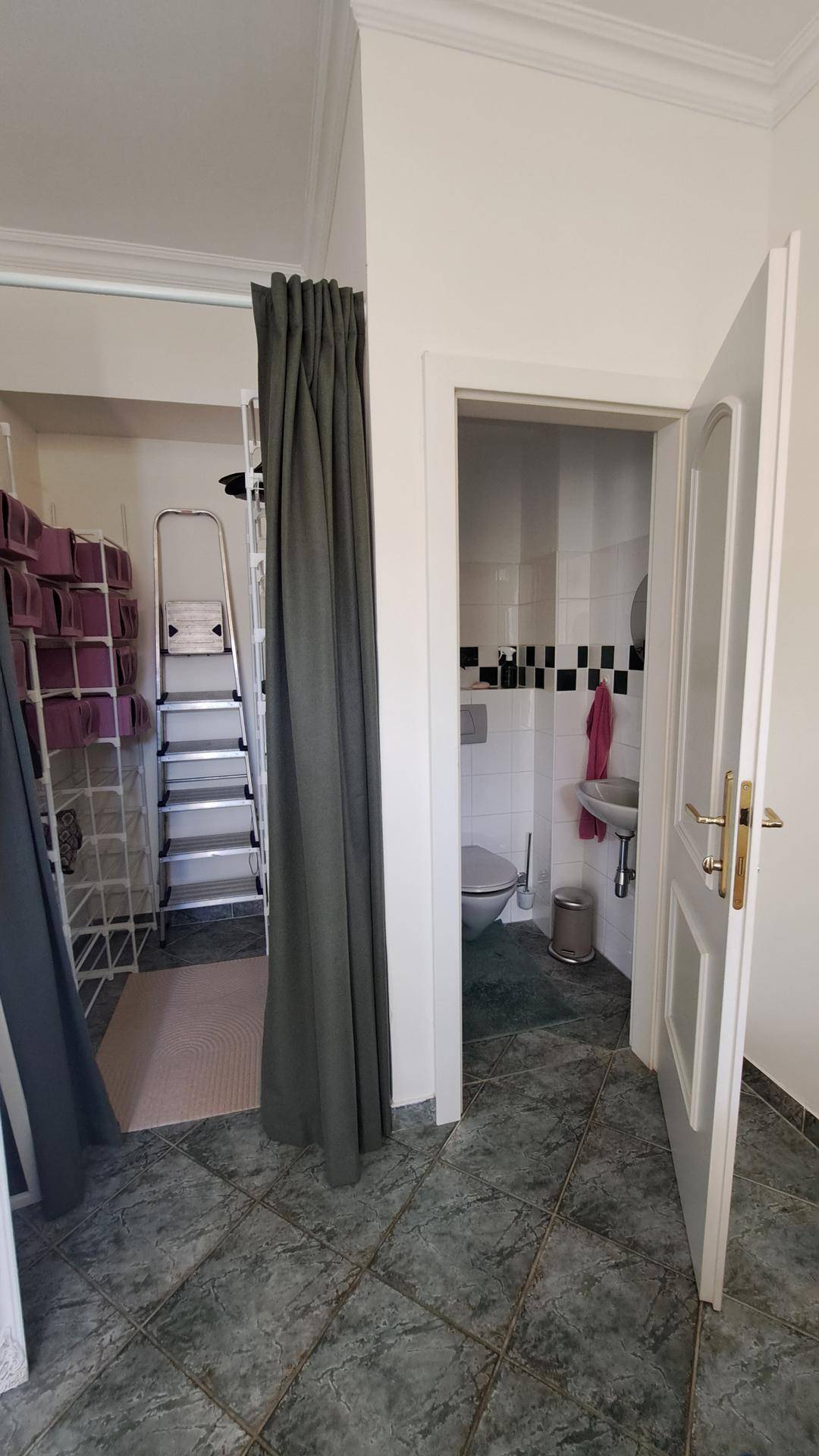 Flur mit Fliesenboden und offener Tür zu einem kleinen Badezimmer oder Gäste-WC.