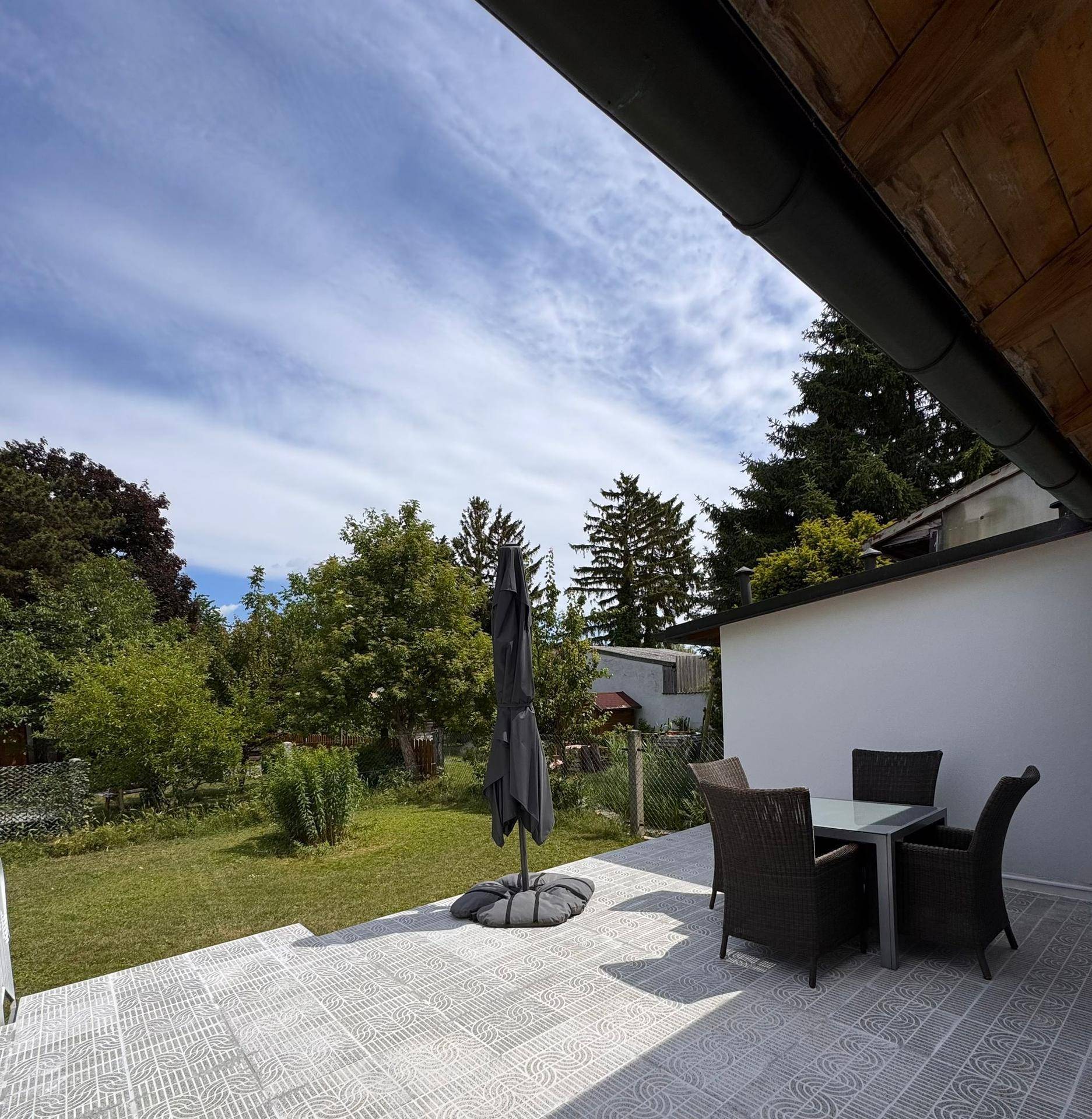 Geräumige Terrasse mit Outdoor-Möbeln und Sonnenschirm, umgeben von viel Grün.