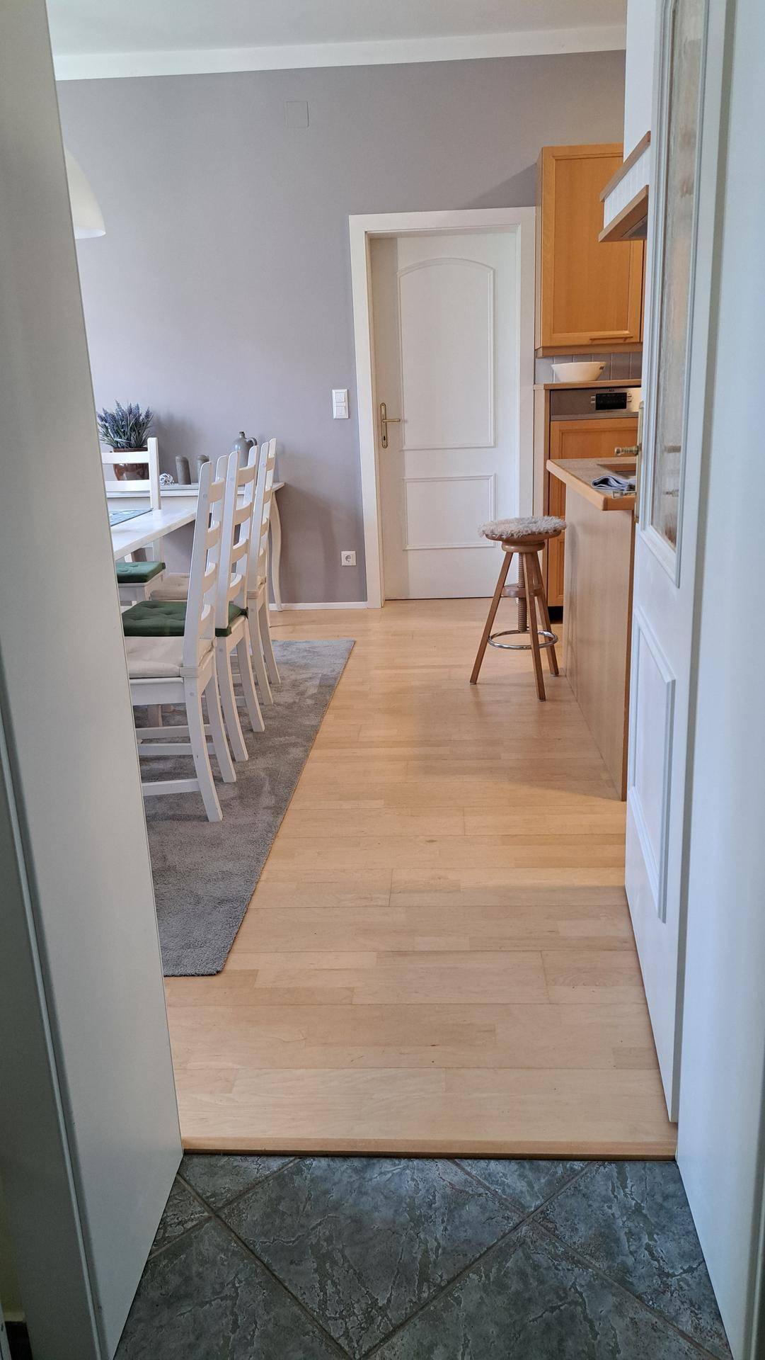 Übergang vom gefliesten Flur zum offenen Küchen- und Essbereich mit Holzfußboden.