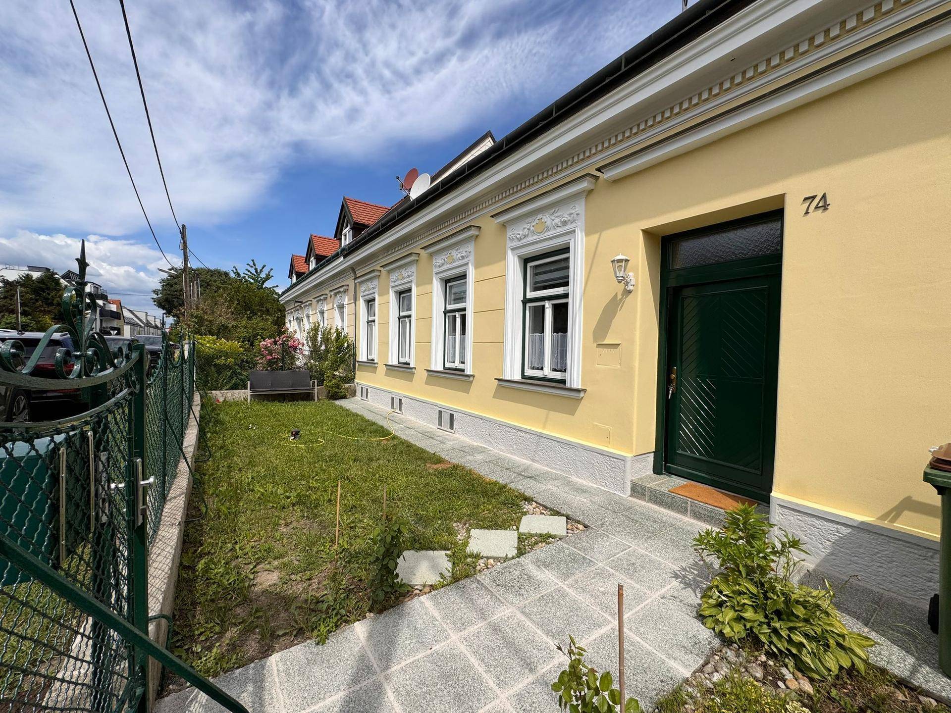 Ansicht der gelben Hausfassade mit gepflegtem Vorgarten und grüner Eingangstür.