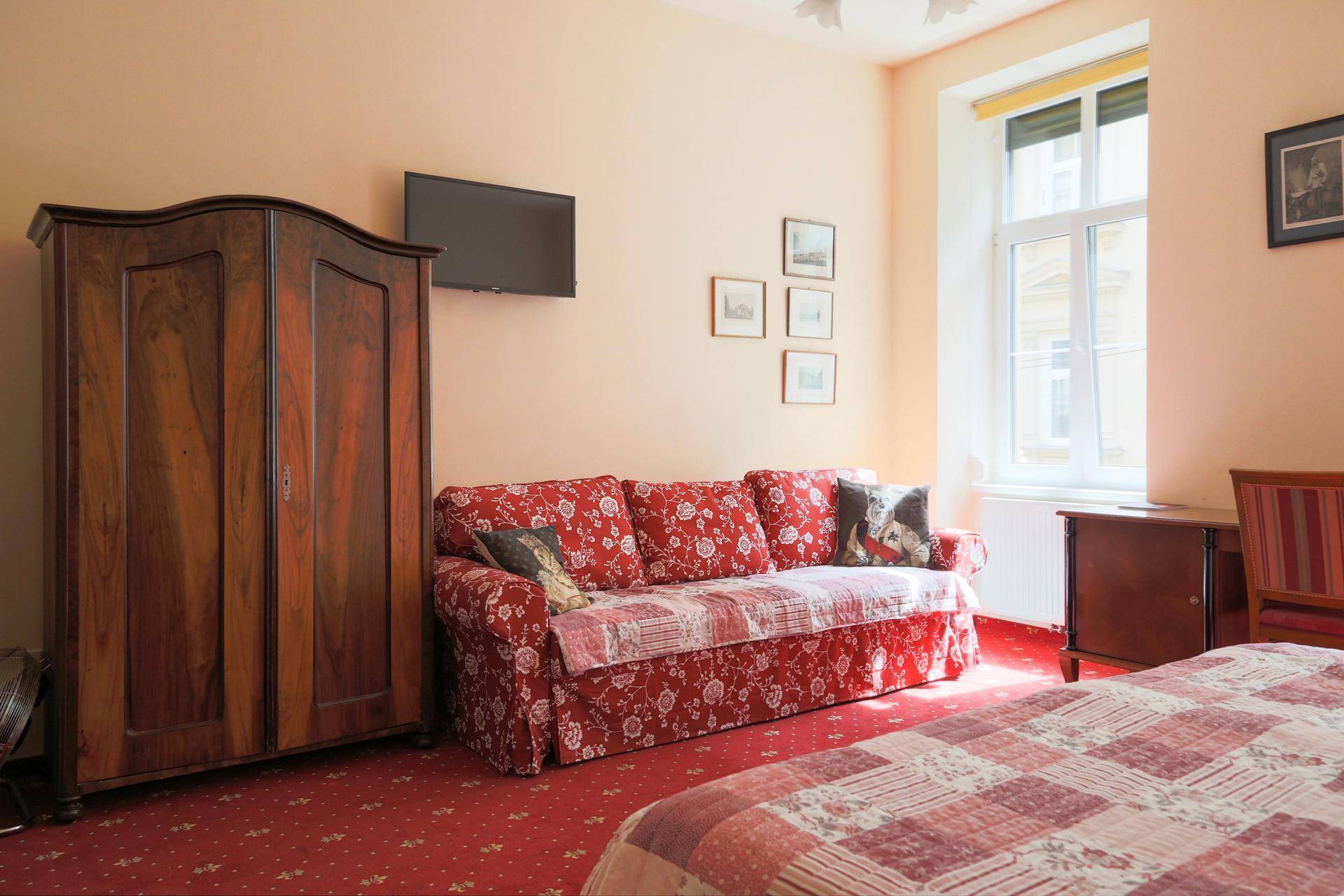 Schlafzimmer mit großem Holzschrank, rotem Teppichboden und einem an der Wand montierten Fernseher.