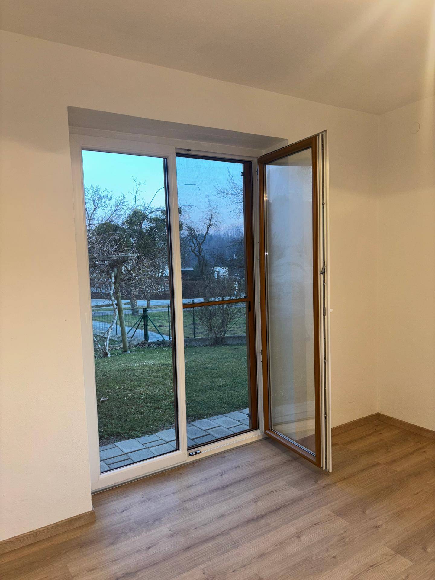 Heller Raum mit Laminatboden und großem Fenster mit Blick in den Garten.