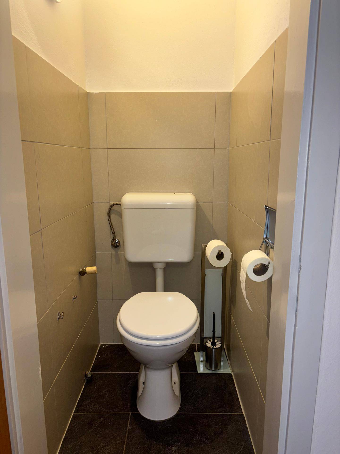 Separate Toilette mit beigefarbenen Fliesen und wandmontierter Toilette.