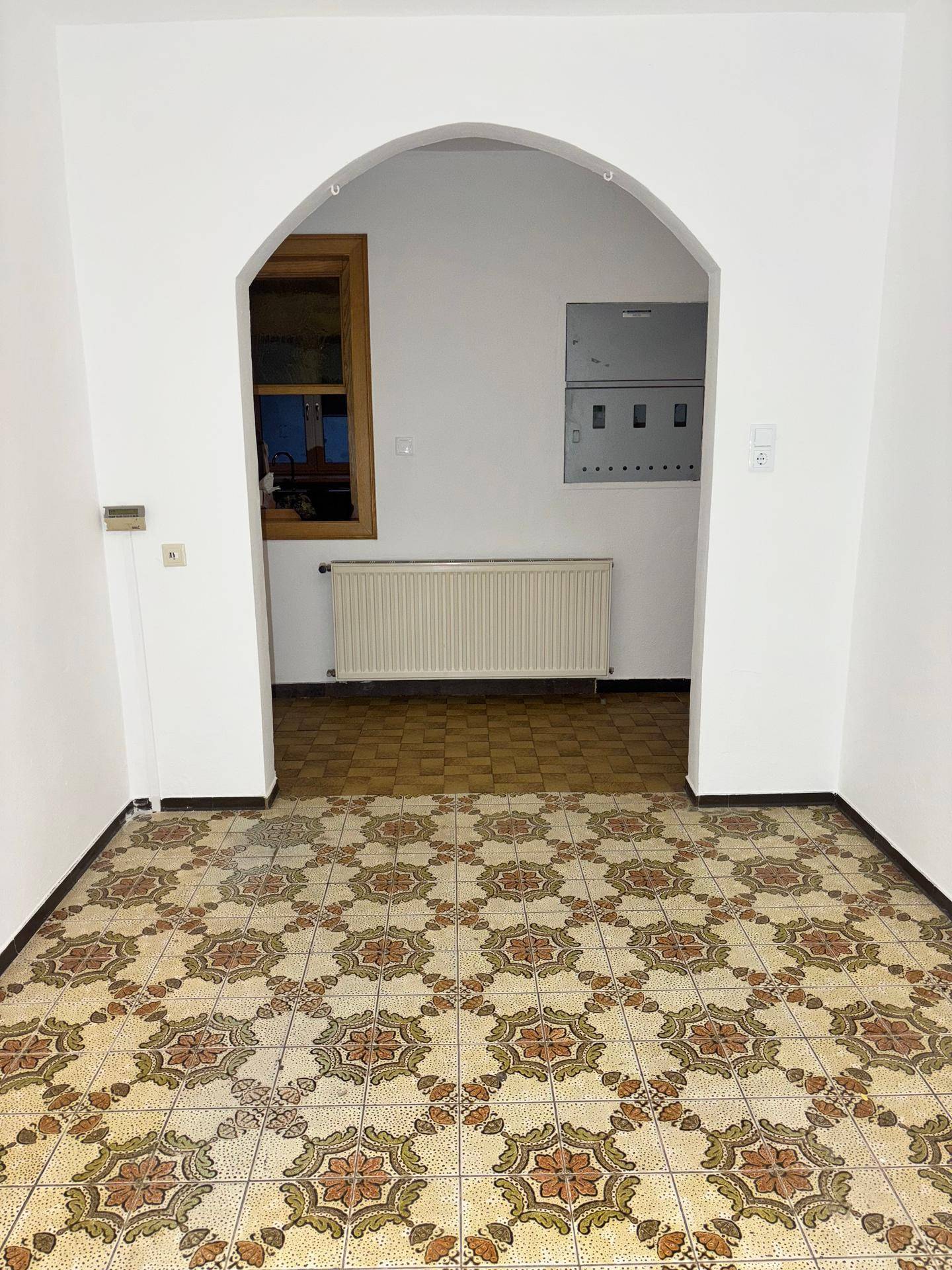 Leerer Raum mit gemusterten Fliesen, Bogenöffnung und Heizkörper.