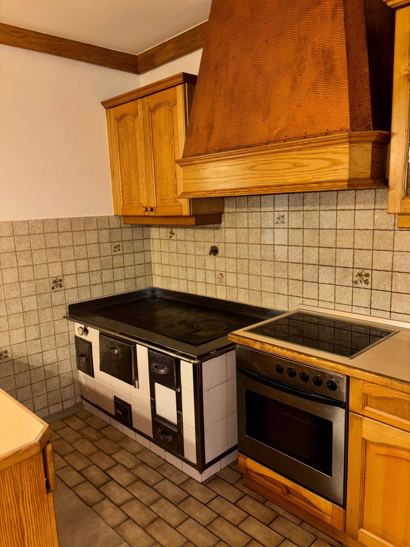 Küche mit traditionellem Holzofen, modernem Kochfeld und Holzschränken.
