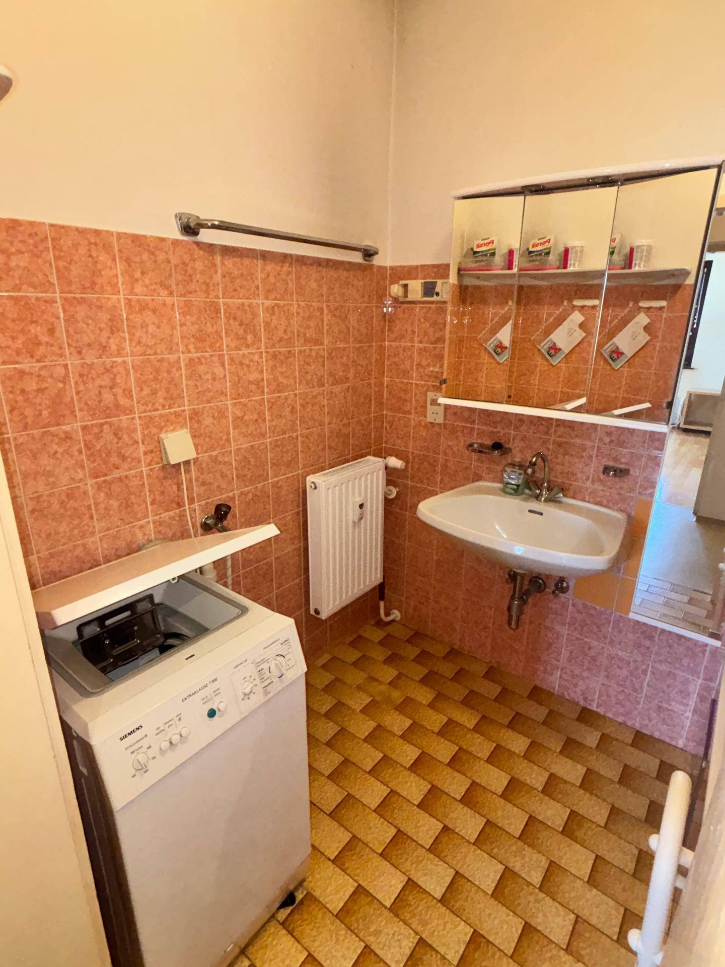 Badezimmer mit Waschbecken, Spiegelschrank und Waschmaschine, ausgestattet mit rosa Fliesen.
