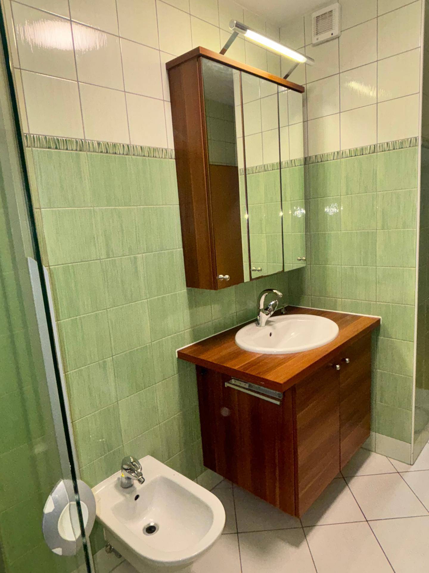 Badezimmer mit grün gefliesten Wänden, Waschbecken, Spiegelschrank und Bidet.