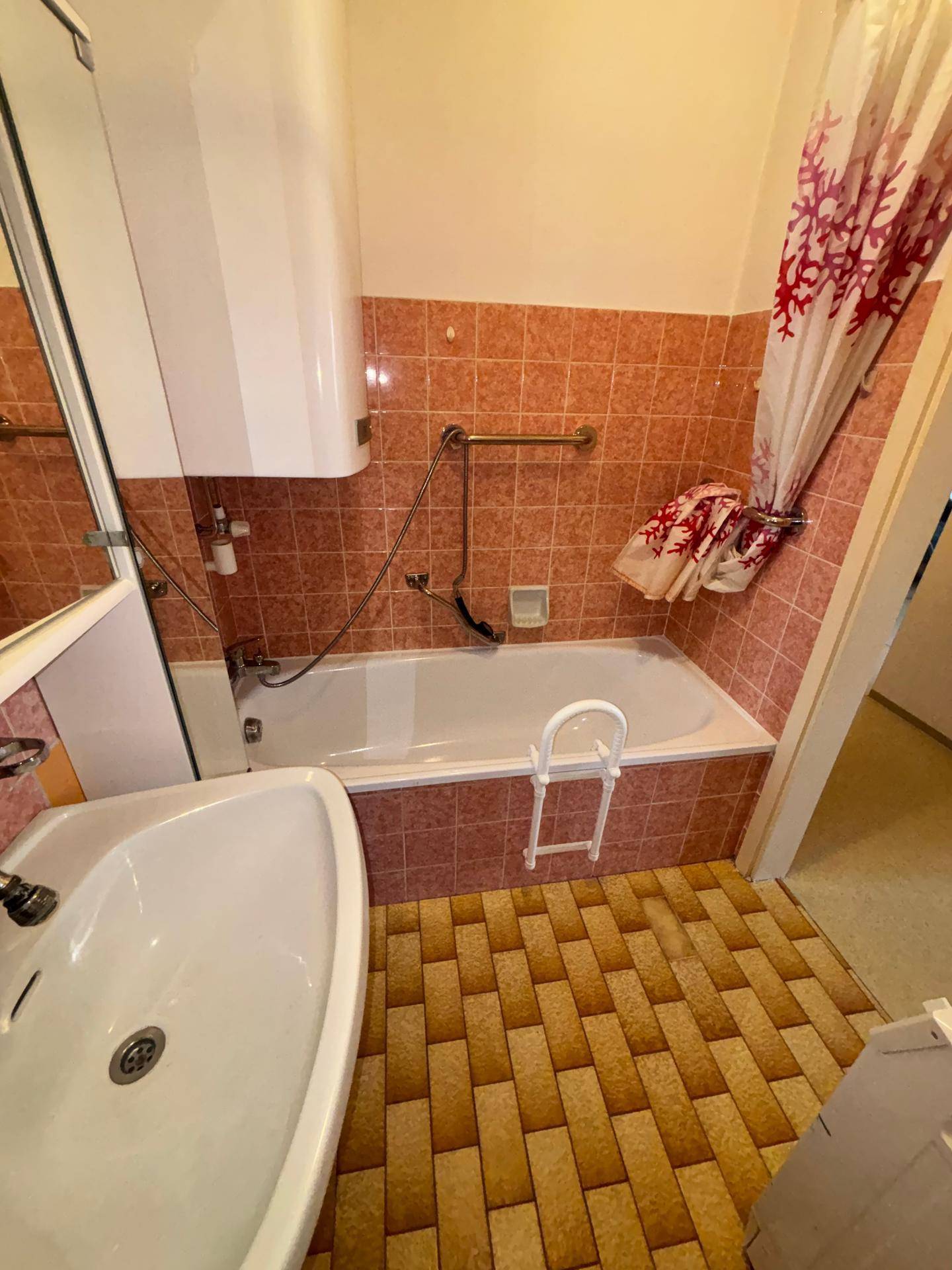 Badezimmer mit Badewanne, Waschbecken und rosa Fliesen, inklusive Haltegriff für Sicherheit.