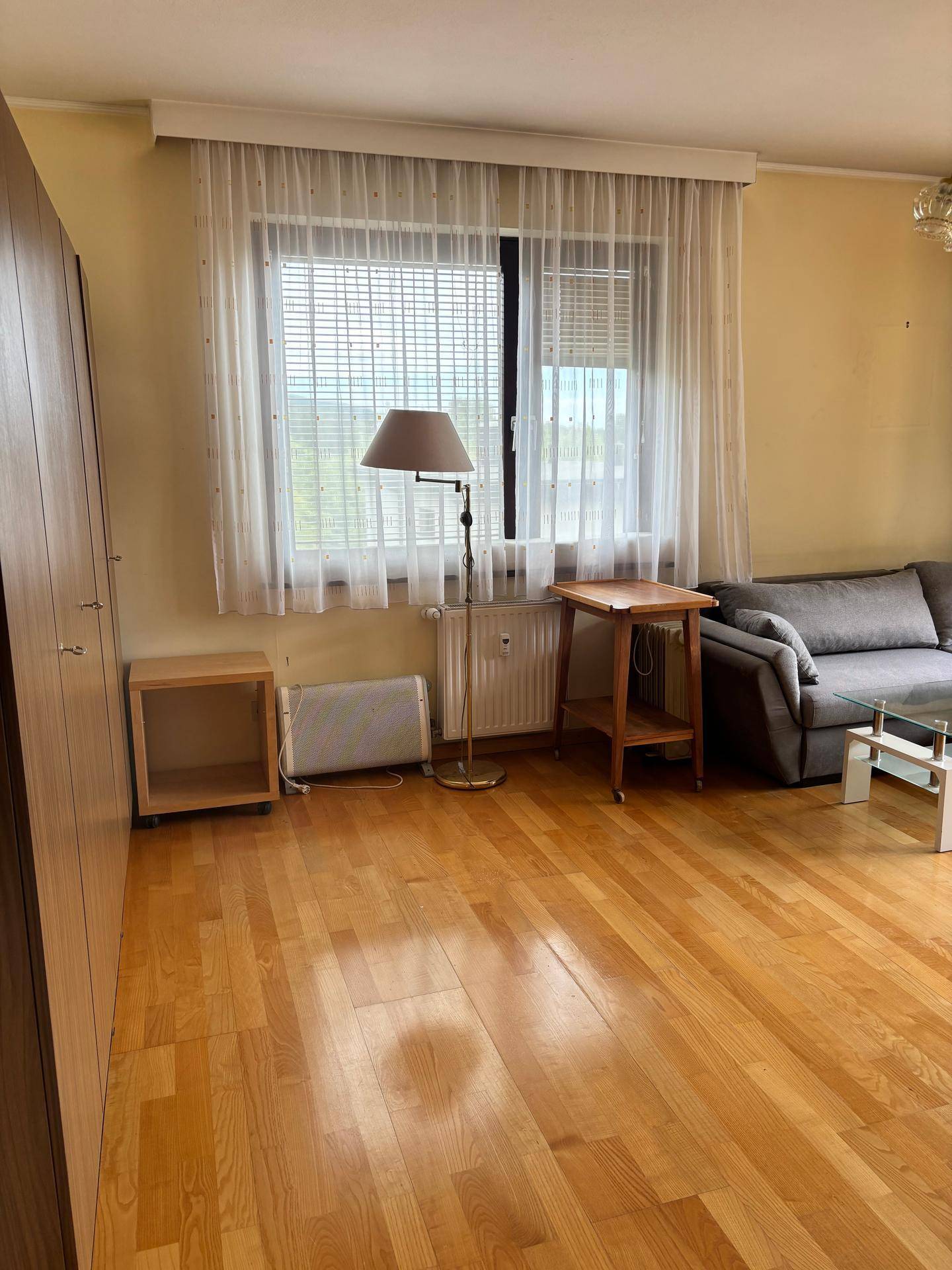 Wohnzimmer mit großem Fenster, Parkettboden und einem praktischen Kleiderschrank.