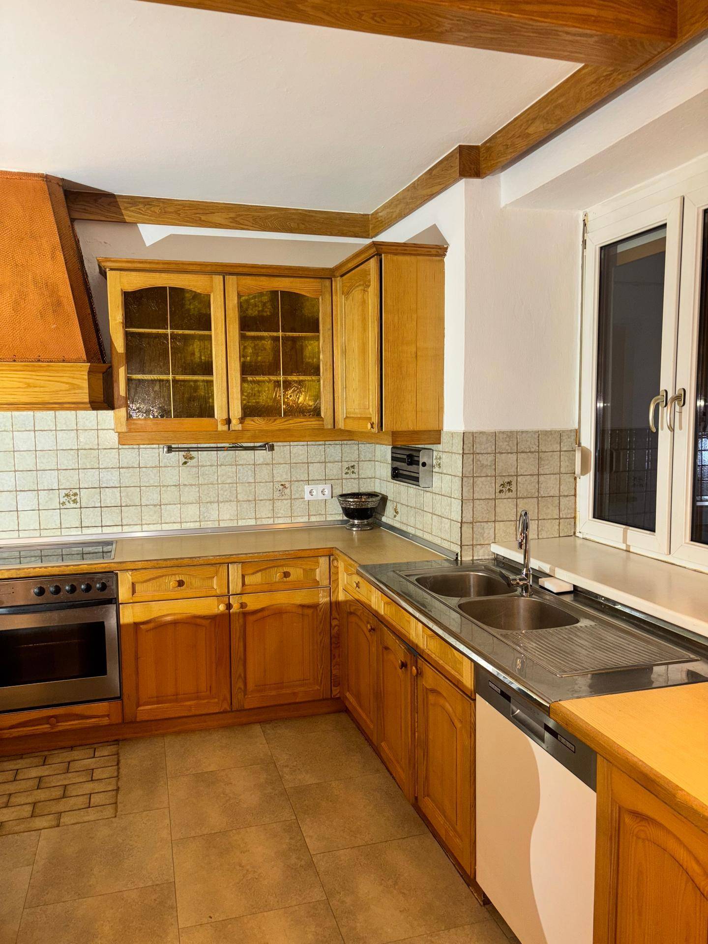 Traditionelle Küche mit Holzschränken, Doppelspüle, Backofen und Fliesenrückwand.