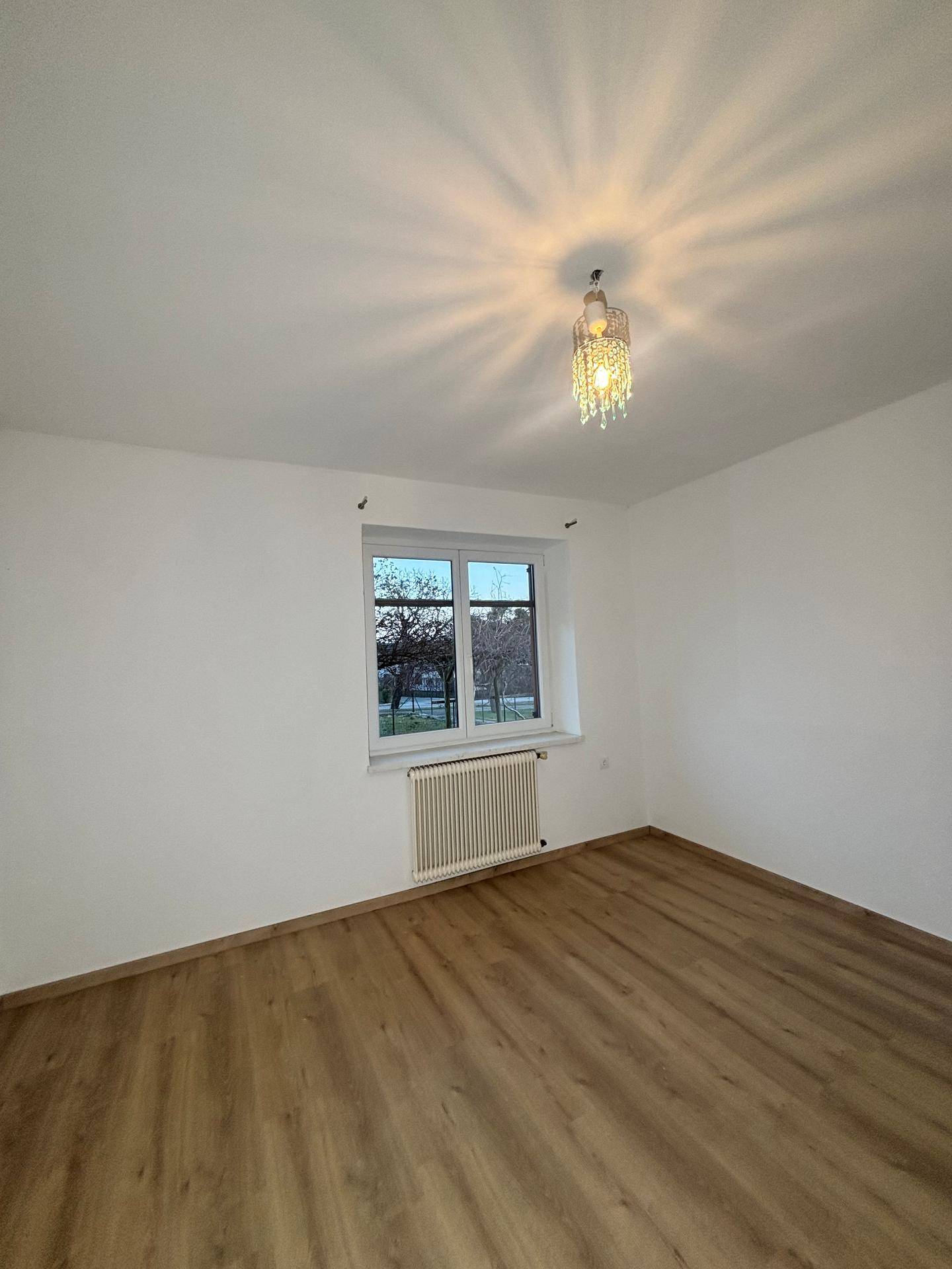 Leerer Raum mit Laminatboden, Fenster und dekorativer Deckenleuchte.
