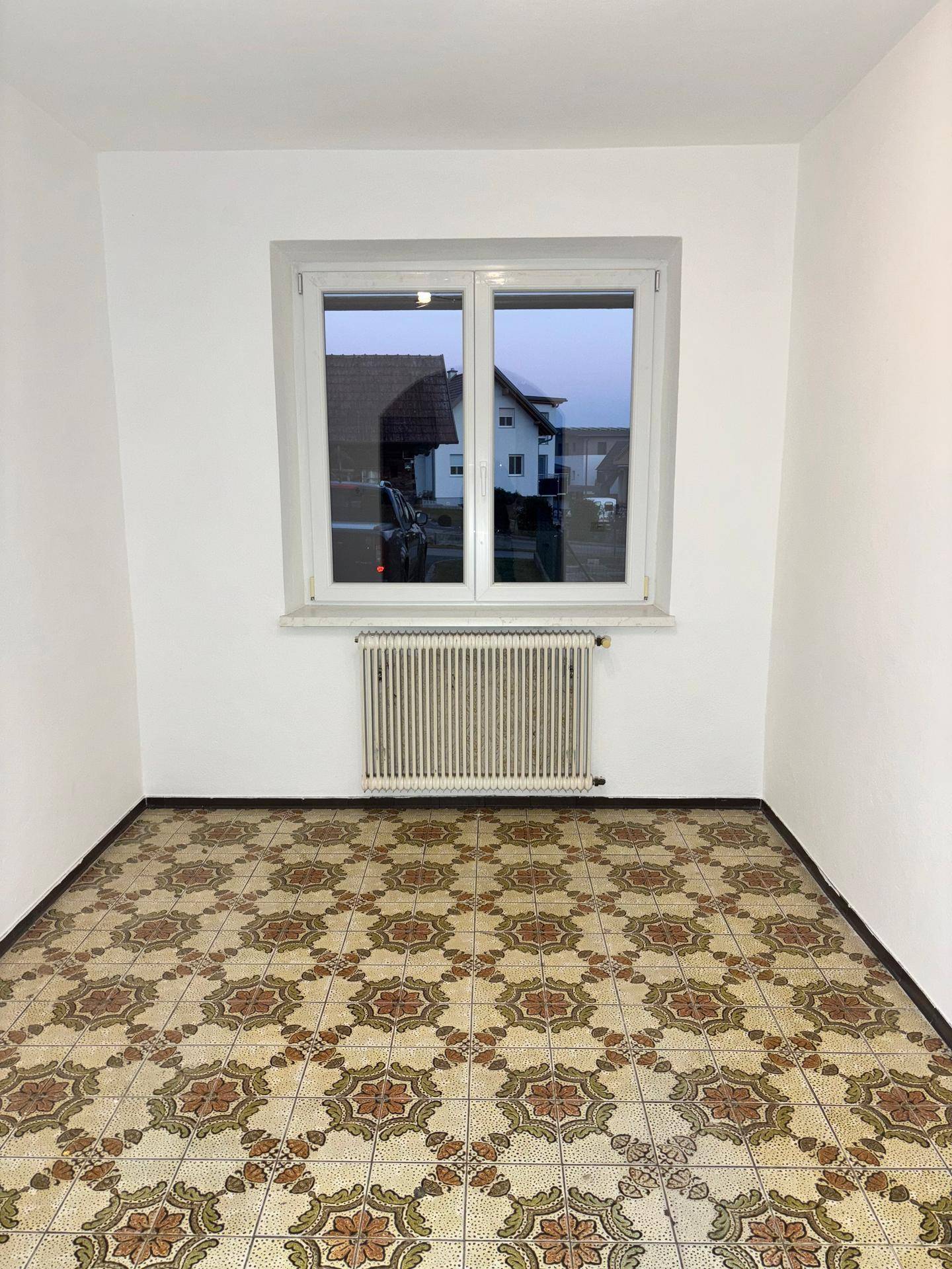 Leerer Raum mit gemusterten Fliesen, Fenster und Heizkörper.