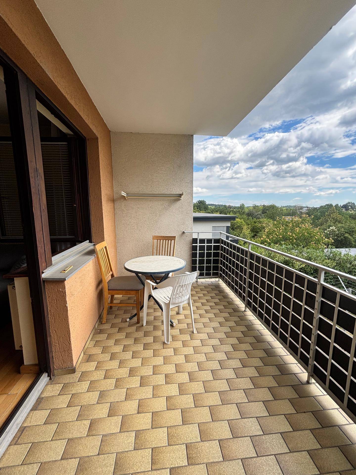 Gemütlicher Balkon mit Fliesenboden, Sitzgelegenheiten und weitem Blick ins Grüne.