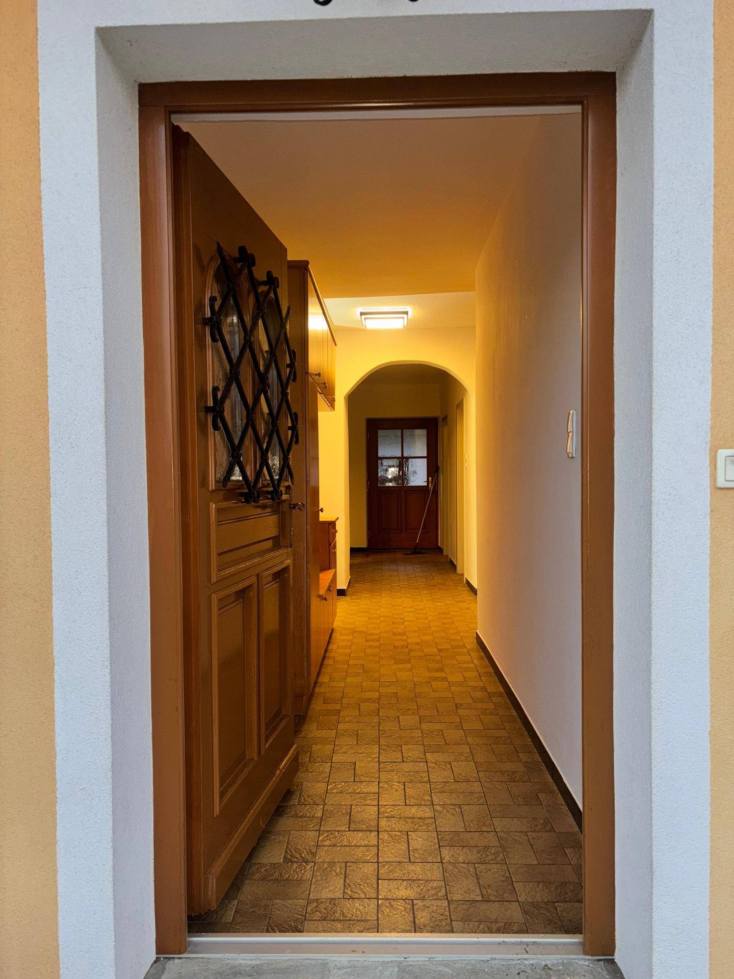 Eingangsbereich mit Holztür, schmiedeeisernem Gitter und gefliestem Boden.
