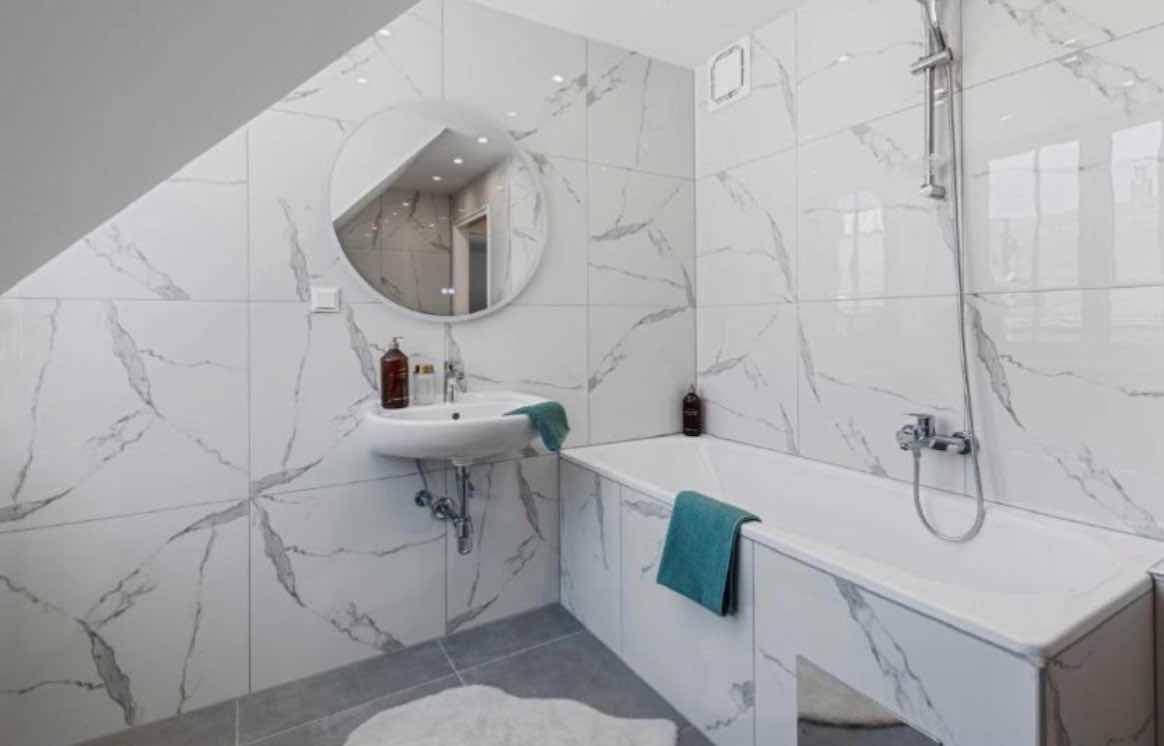 Modernes Badezimmer mit weißen Marmor-Fliesen, Badewanne und Dachschräge.