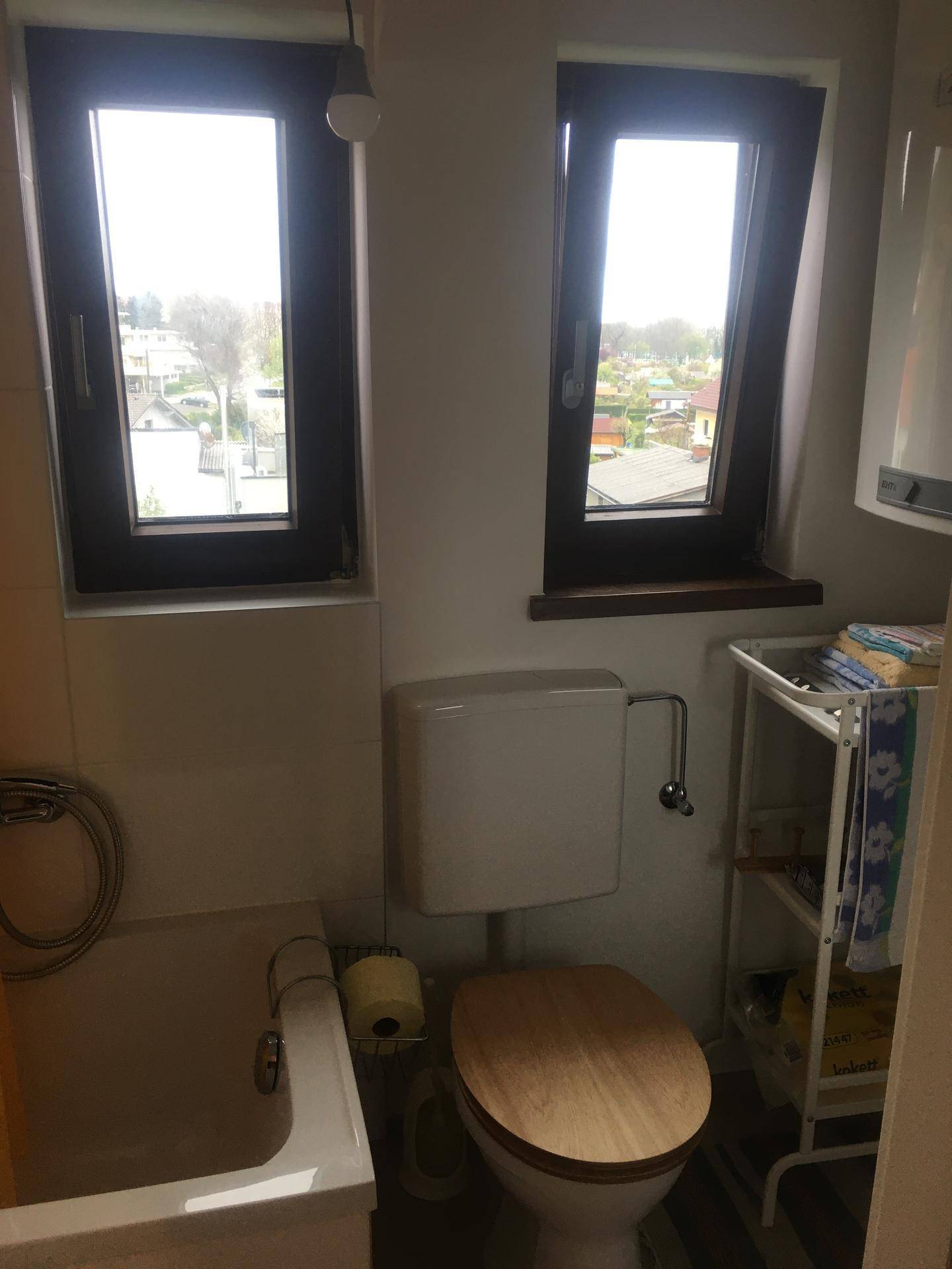 Badezimmer mit Badewanne, Toilette und zwei Fenstern für Tageslicht.