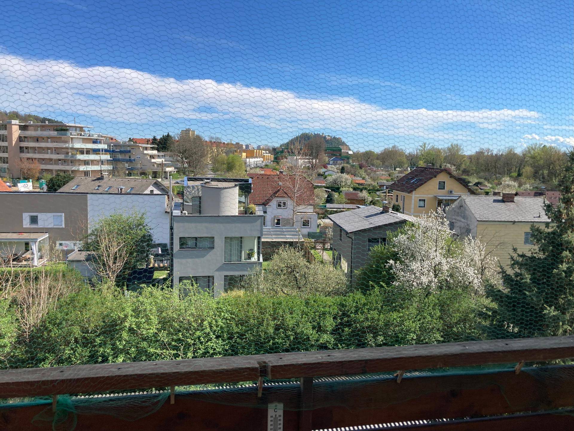 Balkon mit weitem Blick über die Dächer der Stadt und grüne Hügel.