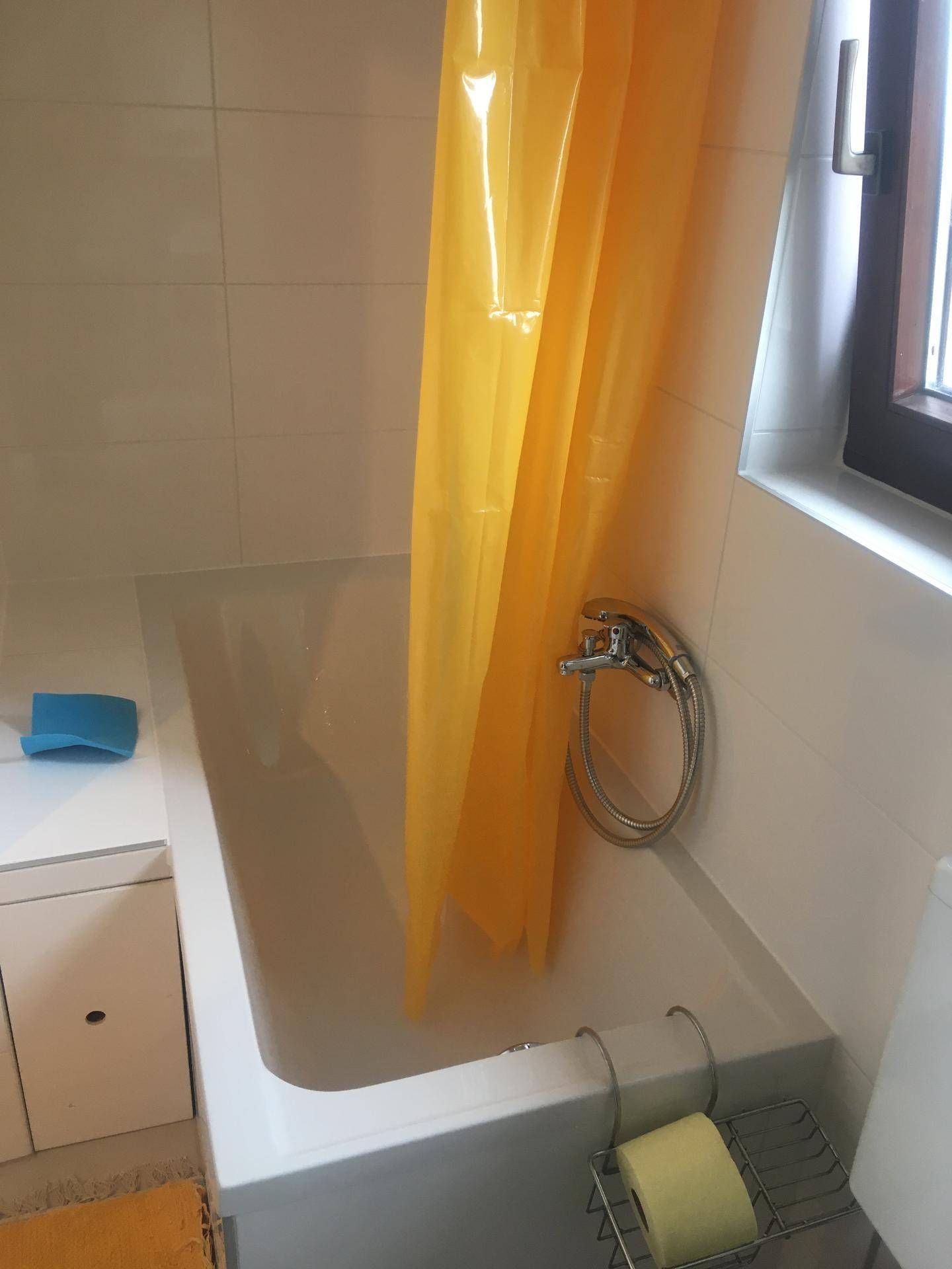 Badezimmer mit Badewanne, Duschvorhang und weißen Fliesen.