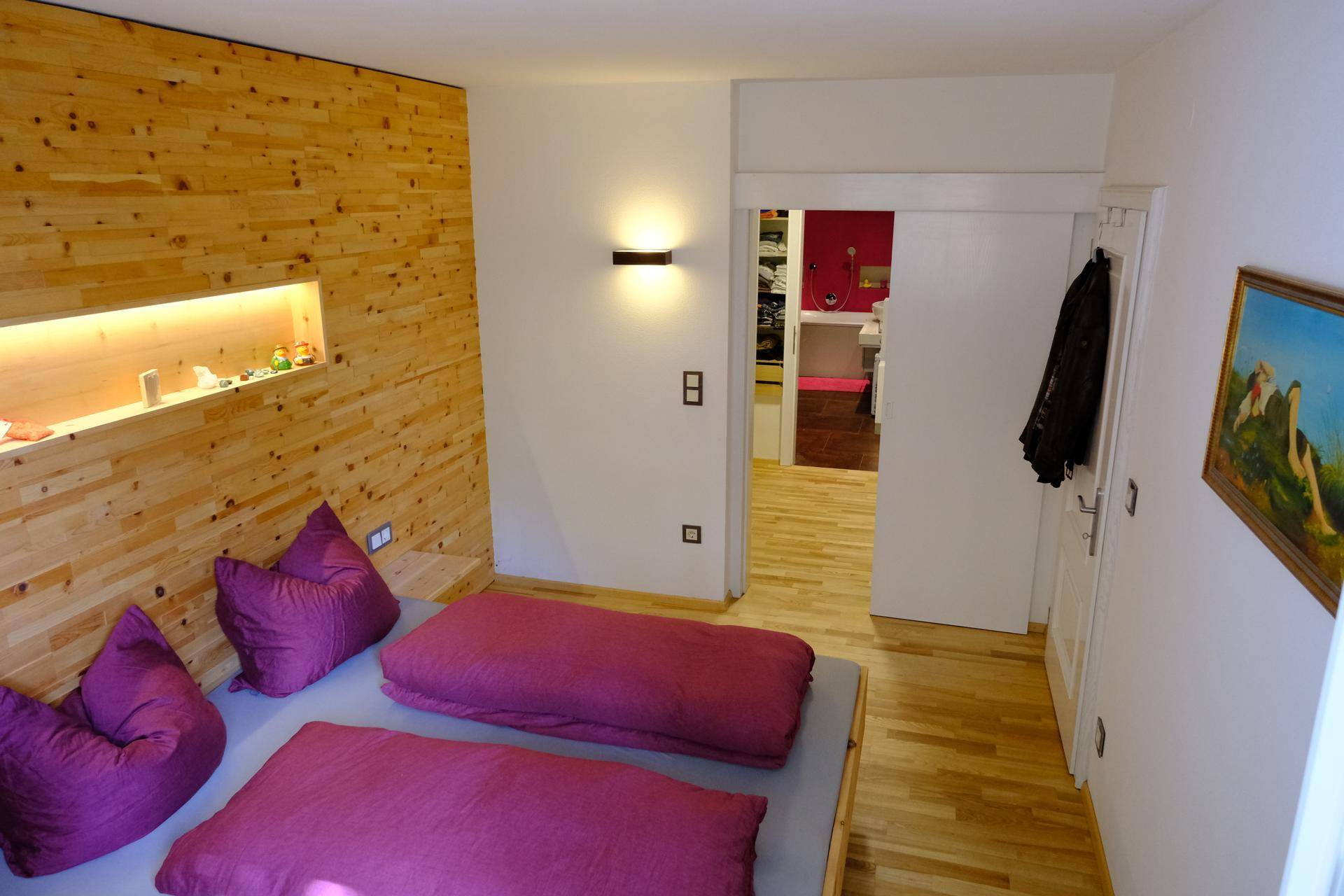 Schlafzimmer mit Holzwand, Holzboden und Zugang zu einem modernen Badezimmer.