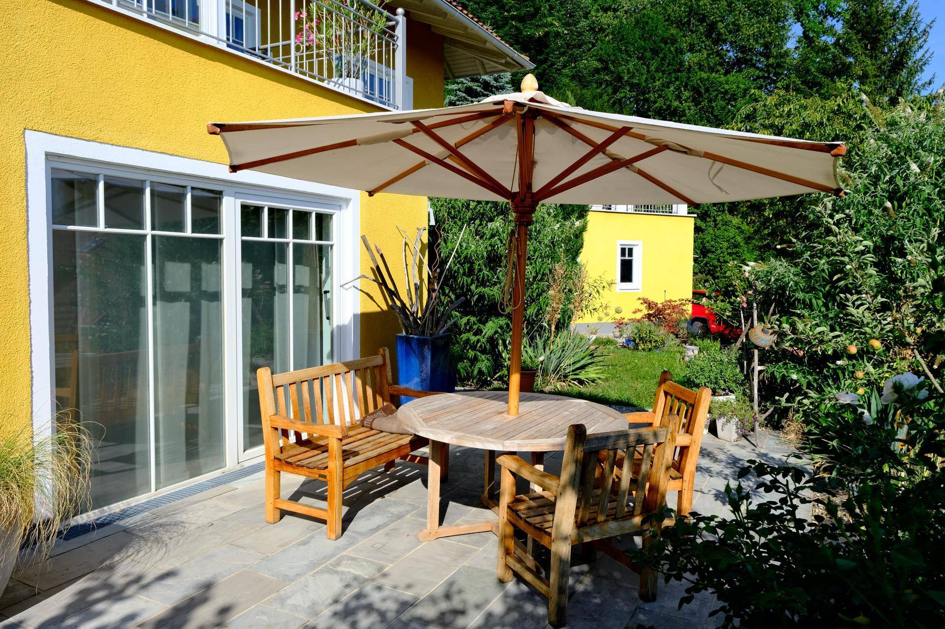 Sonniger Terrassenbereich mit Holzbänken und Tisch, direkt am Haus gelegen.