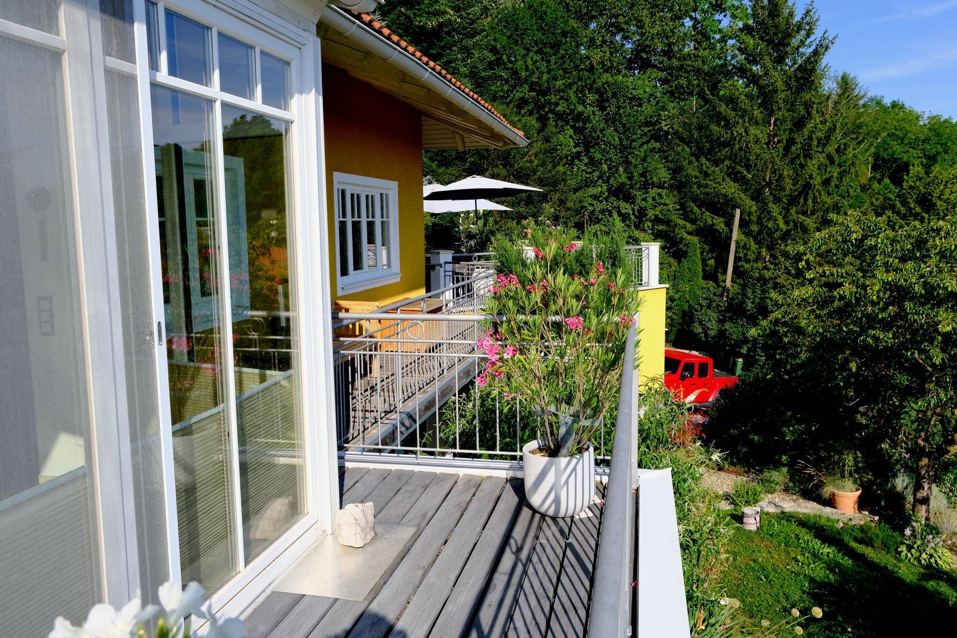 Balkon mit Holzboden und Metallgeländer, umgeben von grüner Natur und Pflanzen.