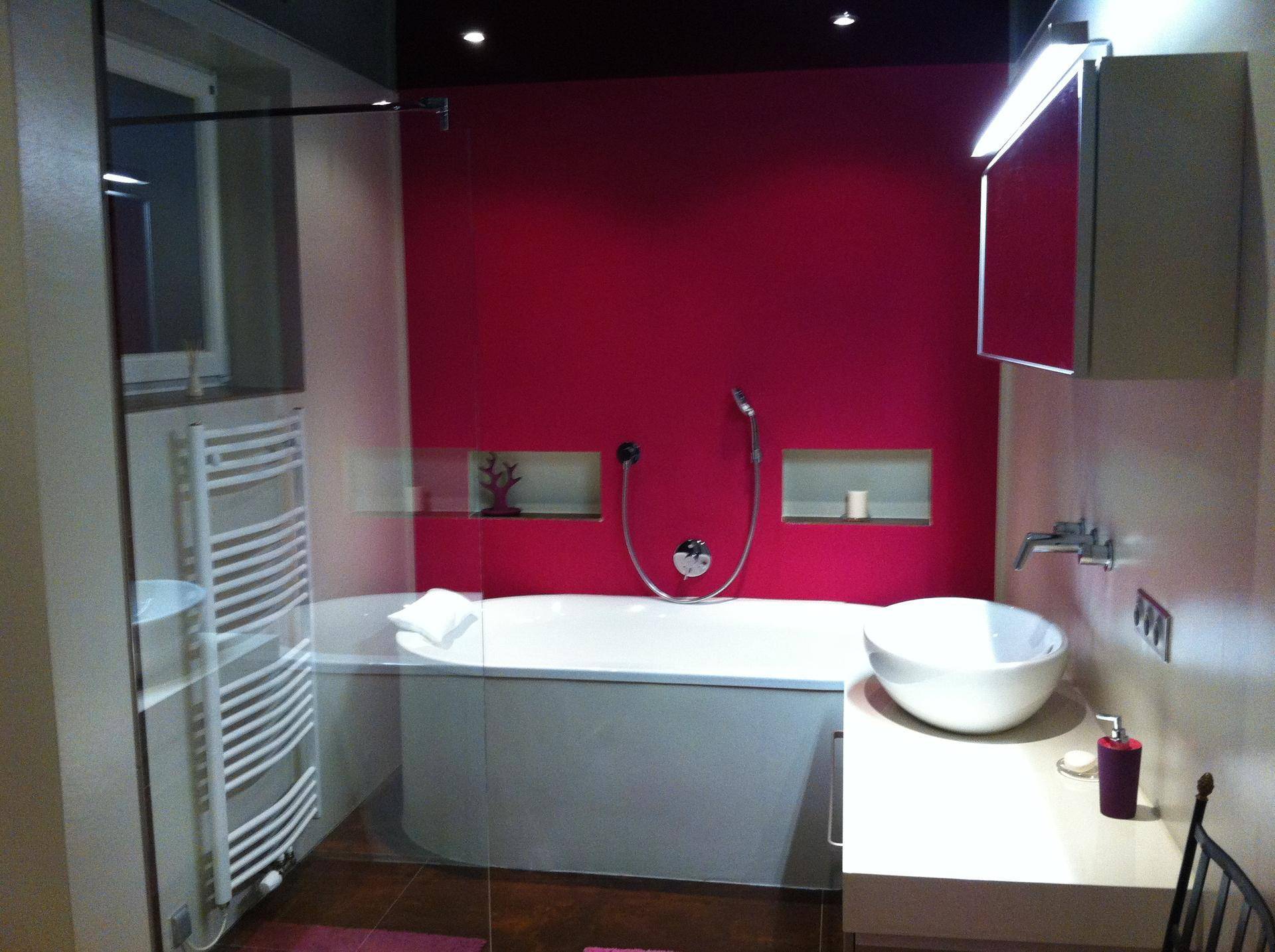Modernes Badezimmer mit pinkfarbener Akzentwand, Badewanne und ovalem Waschbecken.