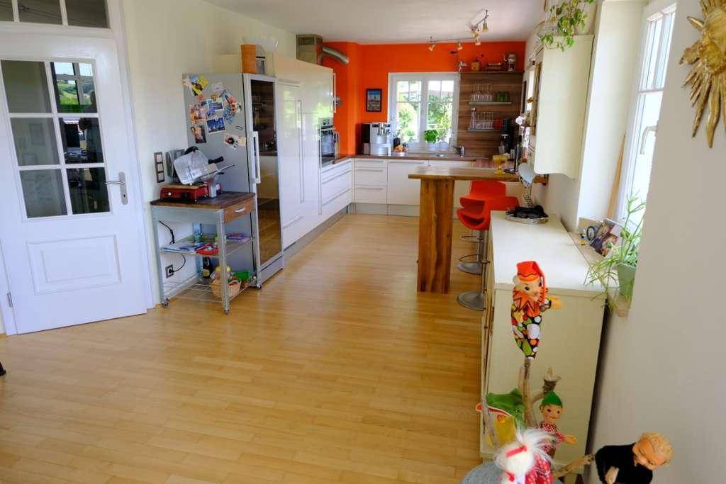Moderne Küche mit weißen Schränken, Holzboden und orangefarbener Akzentwand.