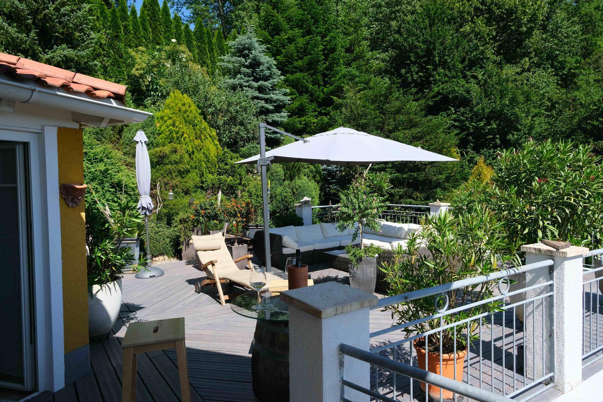 Geräumige Holzterrasse mit Lounge-Möbeln, Sonnenschirm und üppiger Bepflanzung.
