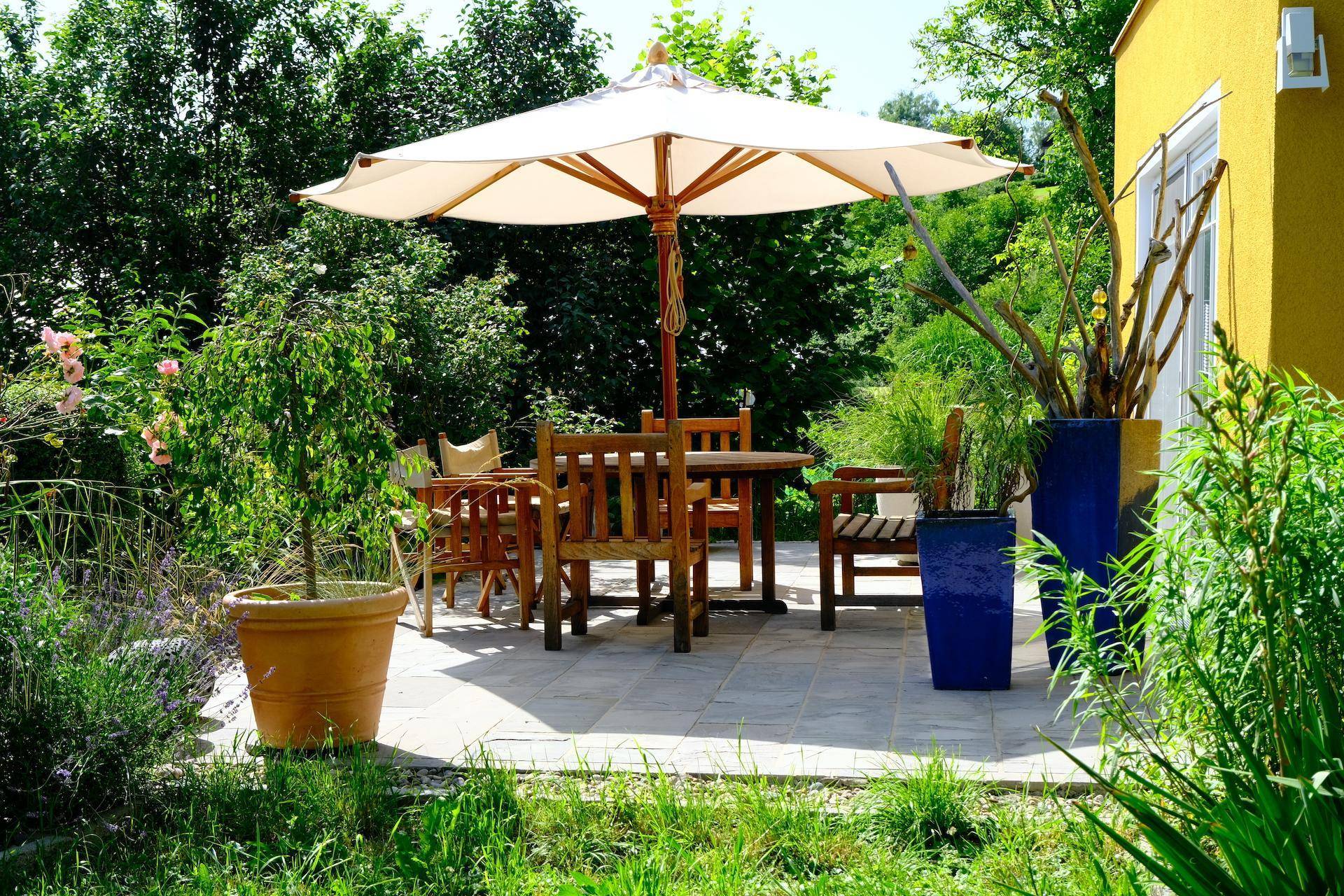 Gemütlicher Essbereich im Garten mit Holztisch, Stühlen und großem Sonnenschirm.
