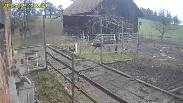 Überwachungsaufnahme eines ländlichen Anwesens mit Scheune und eingezäuntem Außenbereich im Winter.