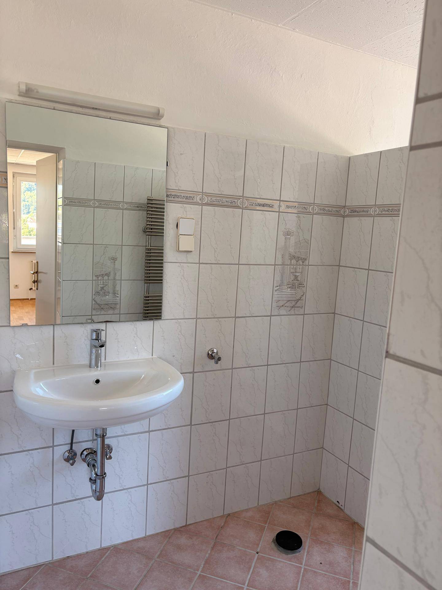 Badezimmer mit weißen Wandfliesen, einem Waschbecken, Spiegel und einem Handtuchheizkörper.