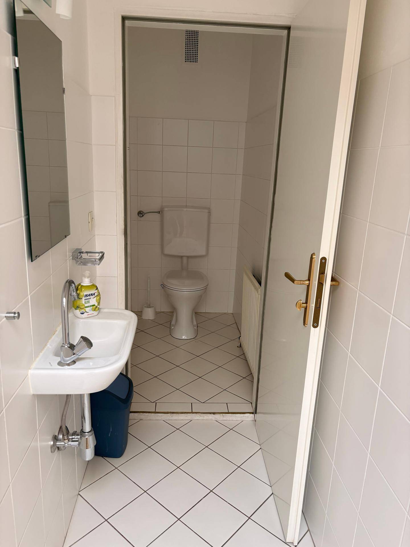 Kleines Badezimmer mit weiß gefliesten Wänden, einem Waschbecken und einer Toilette im Hintergrund.