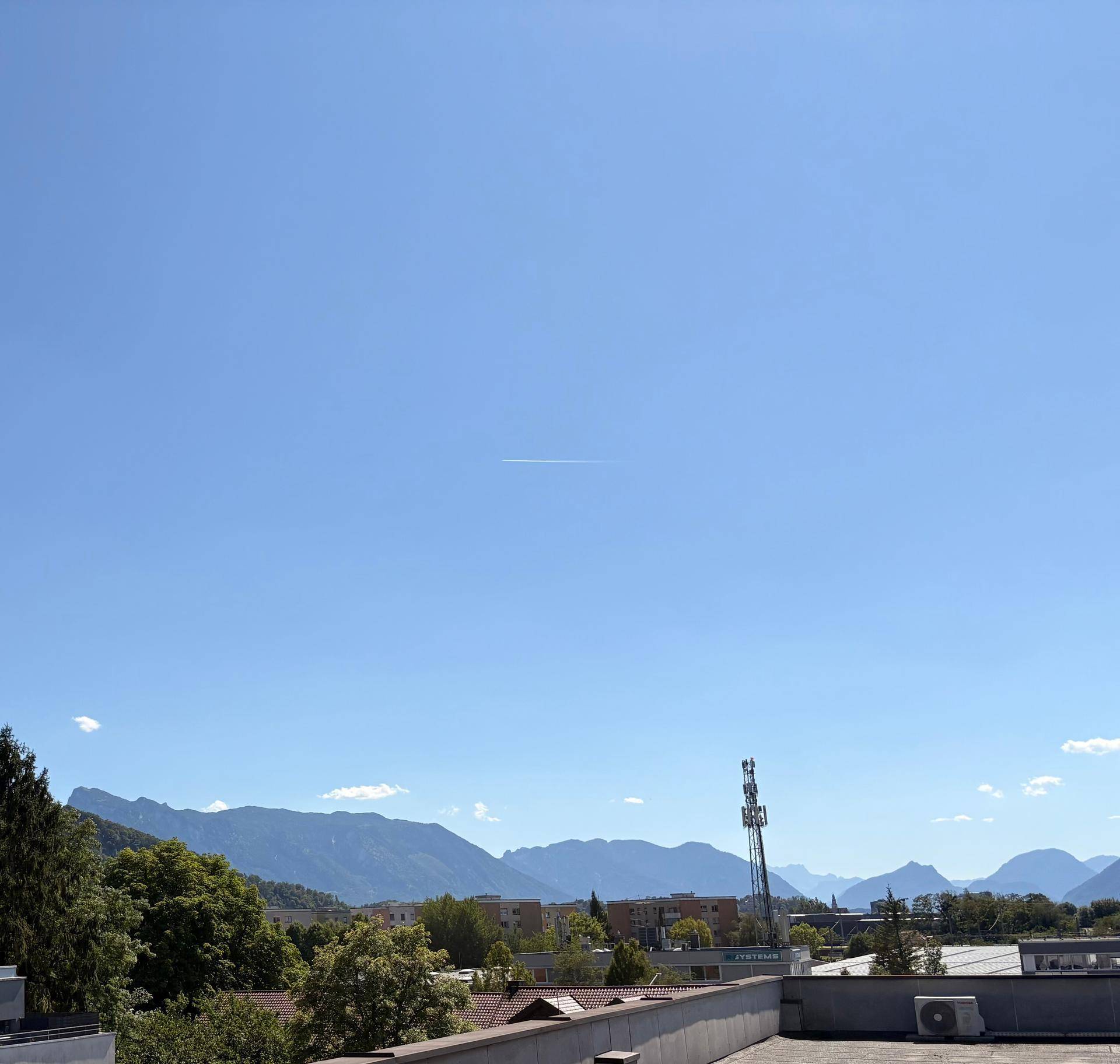 Weitläufiger Blick über eine Stadtlandschaft mit Bergen im Hintergrund unter einem strahlend blauen Himmel.