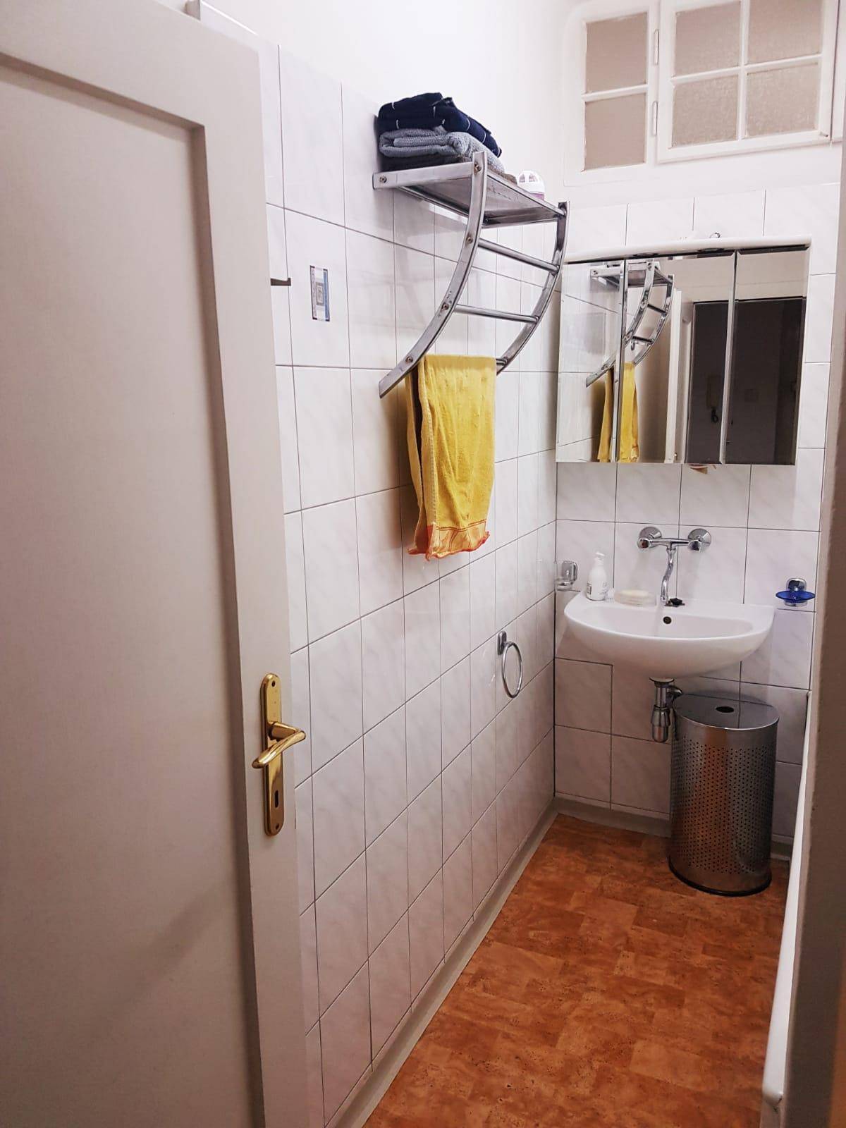 Kleines Badezimmer mit Waschbecken, Spiegel und weißen Fliesen an den Wänden.
