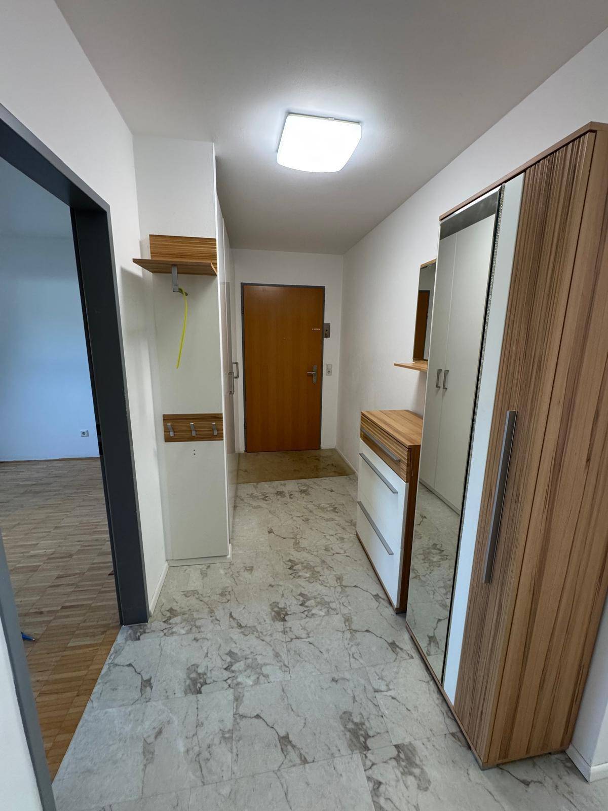 Eingangsbereich mit Steinboden, Garderobe und Spiegelschrank, der zu weiteren Räumen führt.