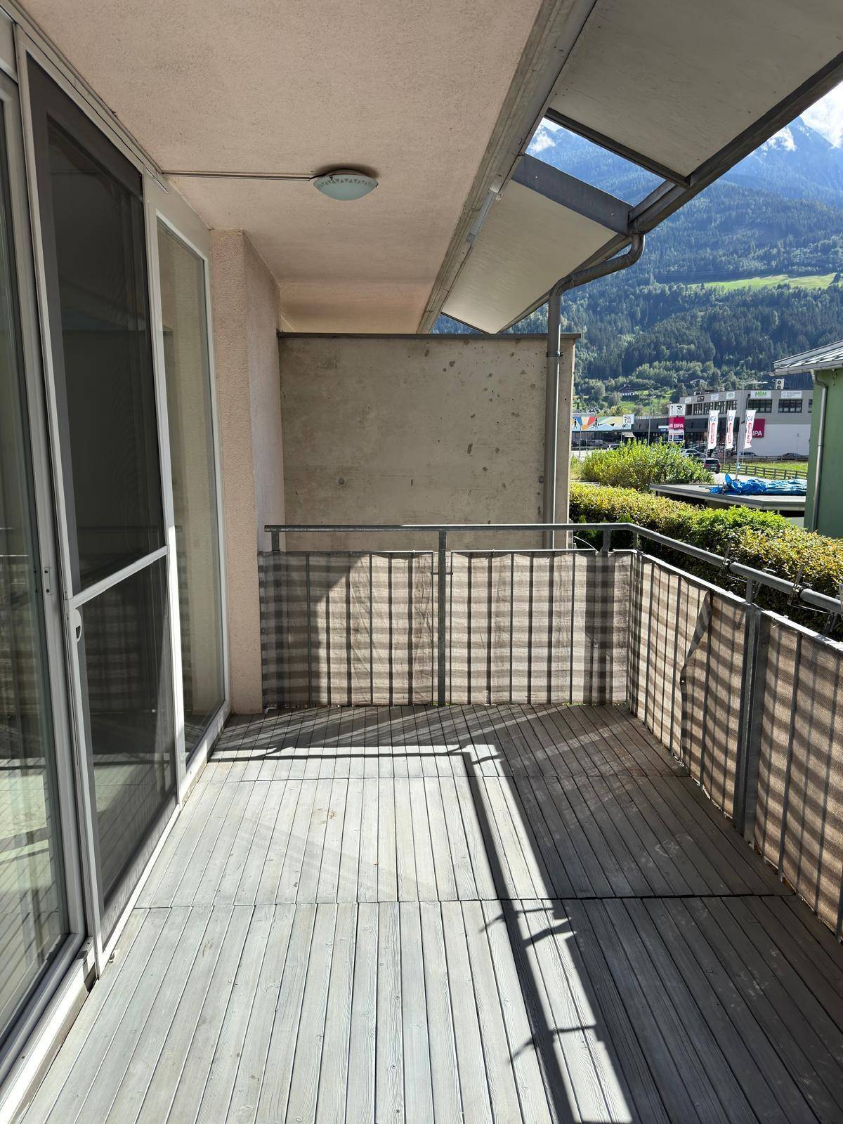 Geräumiger Balkon mit Holzboden und Blick auf die grüne Umgebung und die Berge.