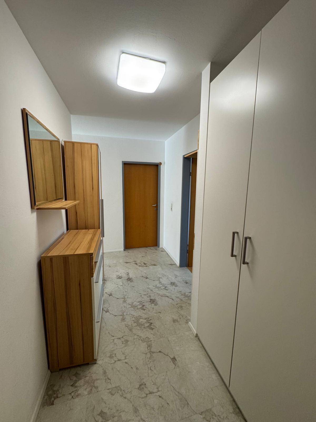 Eingangsbereich mit Garderobe, Spiegel und Schrank, der zu den Wohnräumen führt.