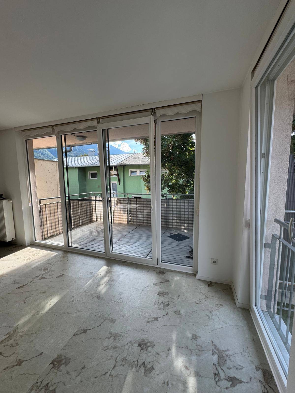 Helles Wohnzimmer mit großflächigen Fenstern, Zugang zum Balkon und Blick auf die Umgebung.