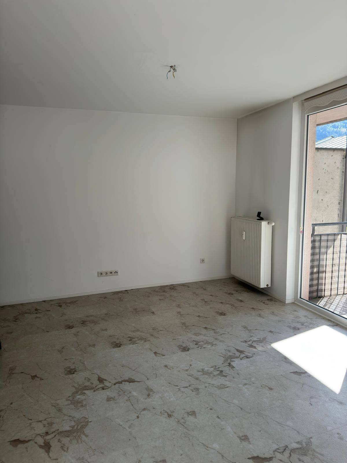 Heller Wohnraum mit Steinboden und Zugang zum Balkon, ideal für entspannte Stunden.