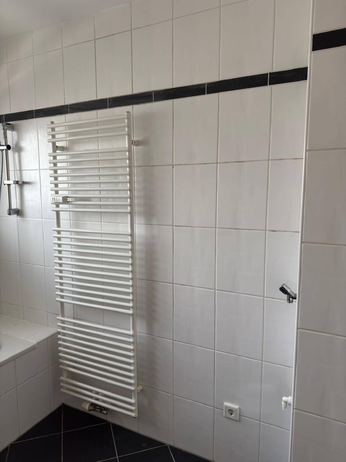 Detailansicht des Badezimmers mit weißem Handtuchheizkörper und weißen Wandfliesen.