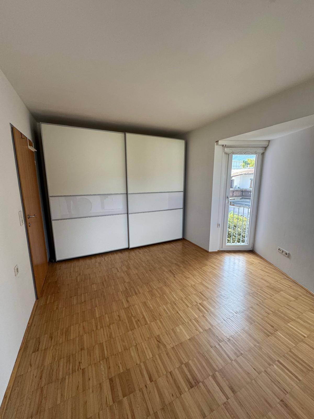 Schlafzimmer mit Parkettboden, großem Schiebeschrank und Zugang zu einem französischen Balkon.