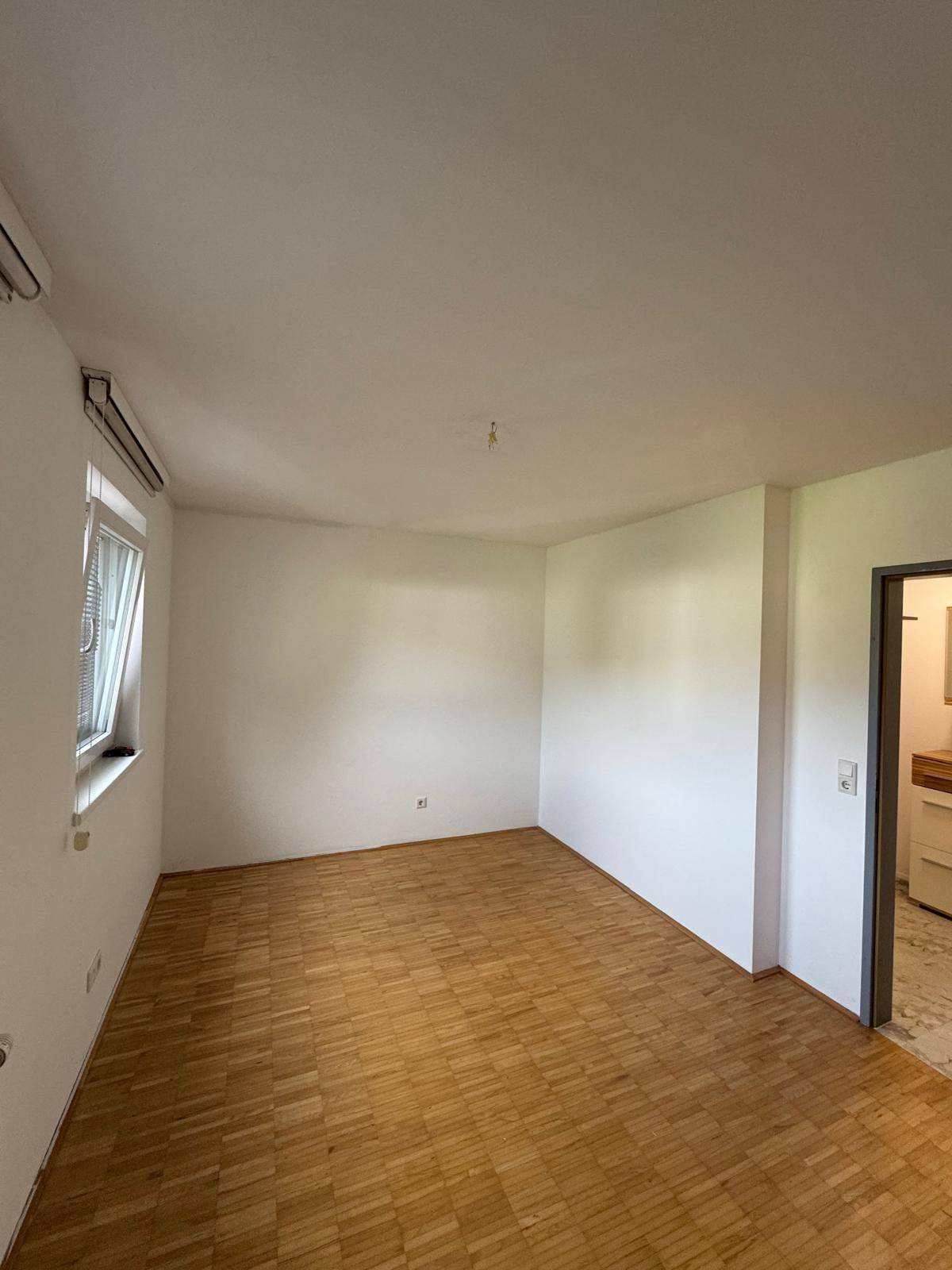 Schlafzimmer mit Parkettboden und Fenster, das viel natürliches Licht hereinlässt.