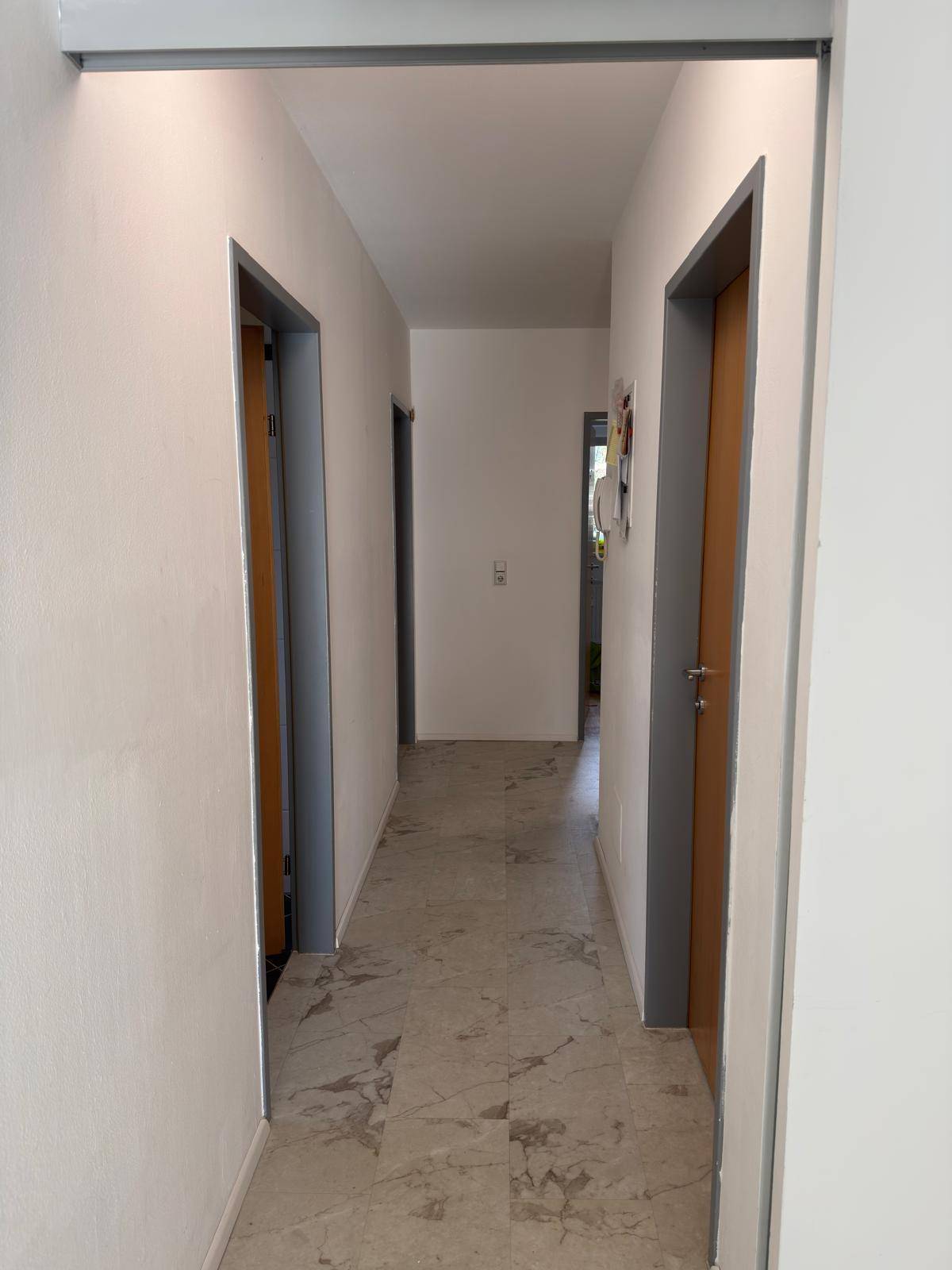 Langer, heller Flur mit Steinboden, der verschiedene Wohnbereiche miteinander verbindet.