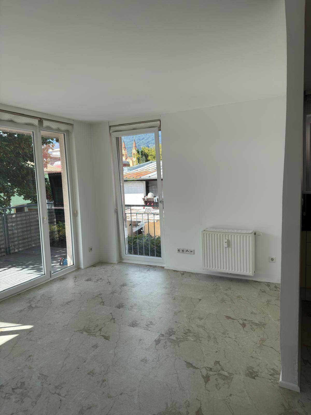 Heller Wohnraum mit Steinboden und Zugang zum Balkon, bietet einen Blick auf die Stadt.