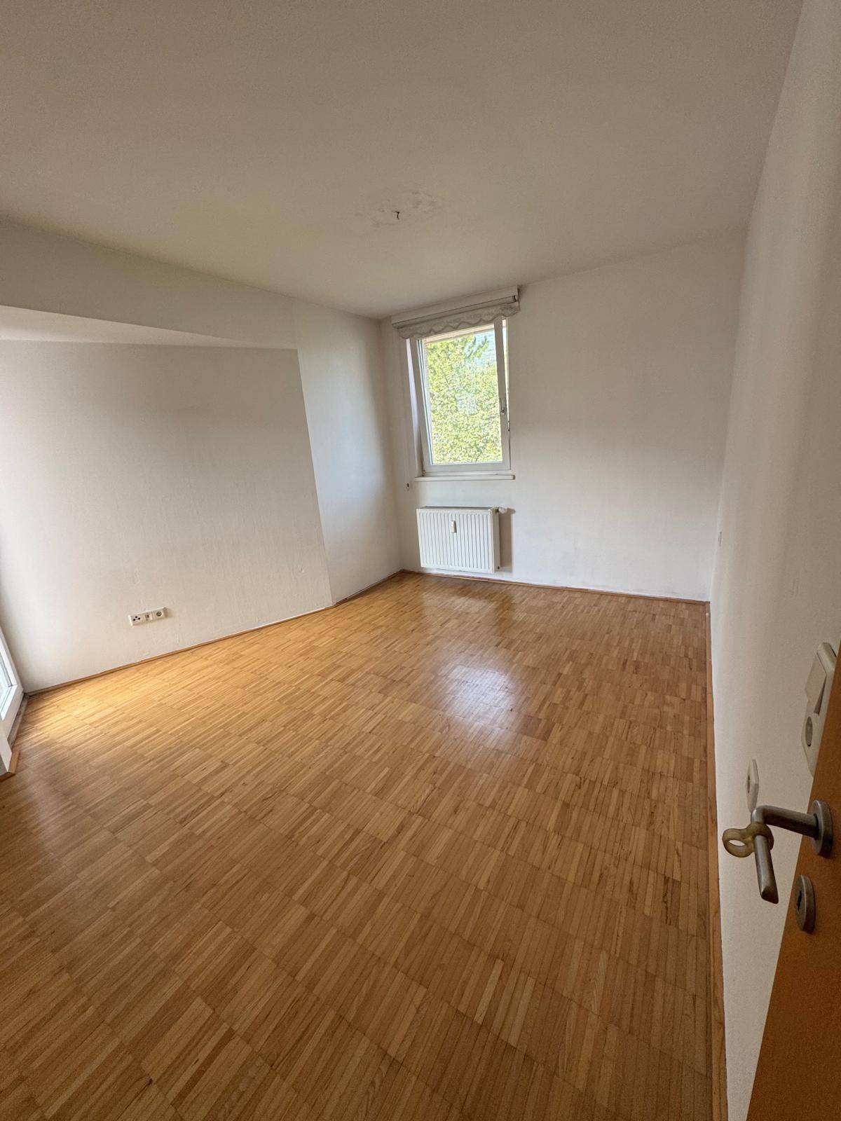 Helles Schlafzimmer mit Parkettboden und Fenster, bereit für persönliche Einrichtung.