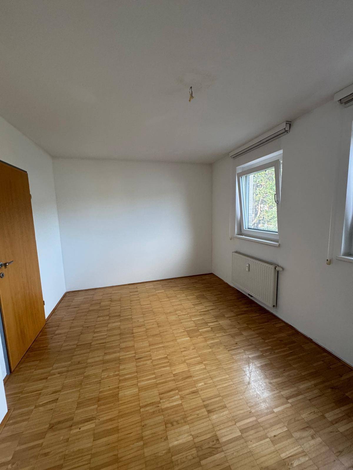Geräumiges Schlafzimmer mit Parkettboden und zwei Fenstern für viel Tageslicht.